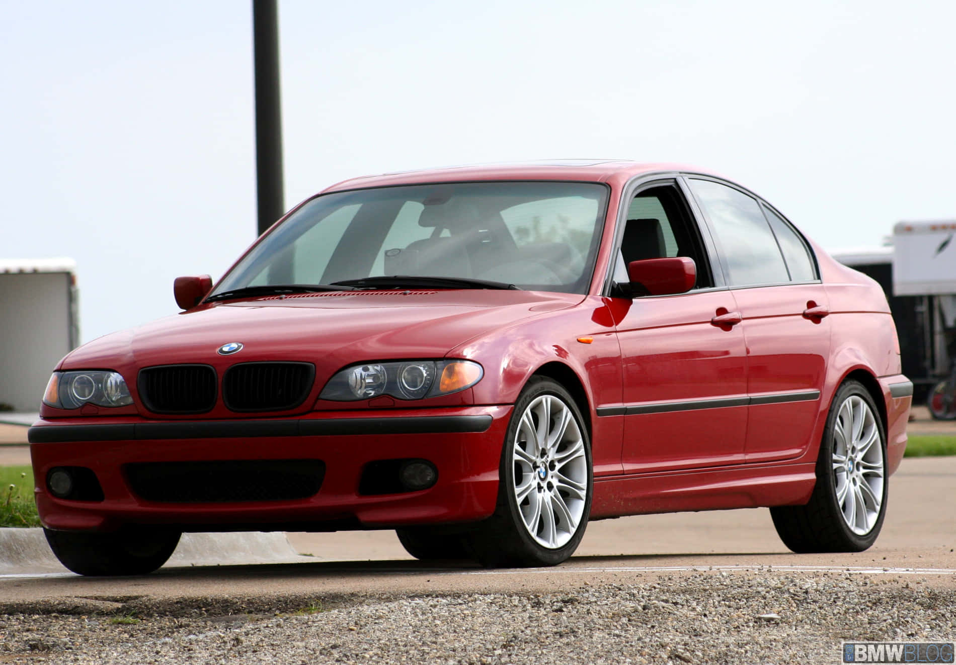 BMW 動圖 桌布 壁紙 — 一輛亮麗的紅色BMW 3系列轎車停在碎石上，配備銀色合金輪圈，在明亮的日光下。