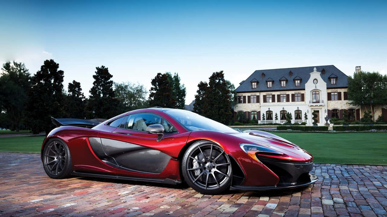 720p Mclaren 720s 桌布 壁紙 — 一輛亮麗的紅色McLaren P1超級跑車停放在磚砌車道上，前方是一座宏偉的歐式豪宅，擁有修剪整齊的草坪和高大的樹木，背景是清澈的藍天。
