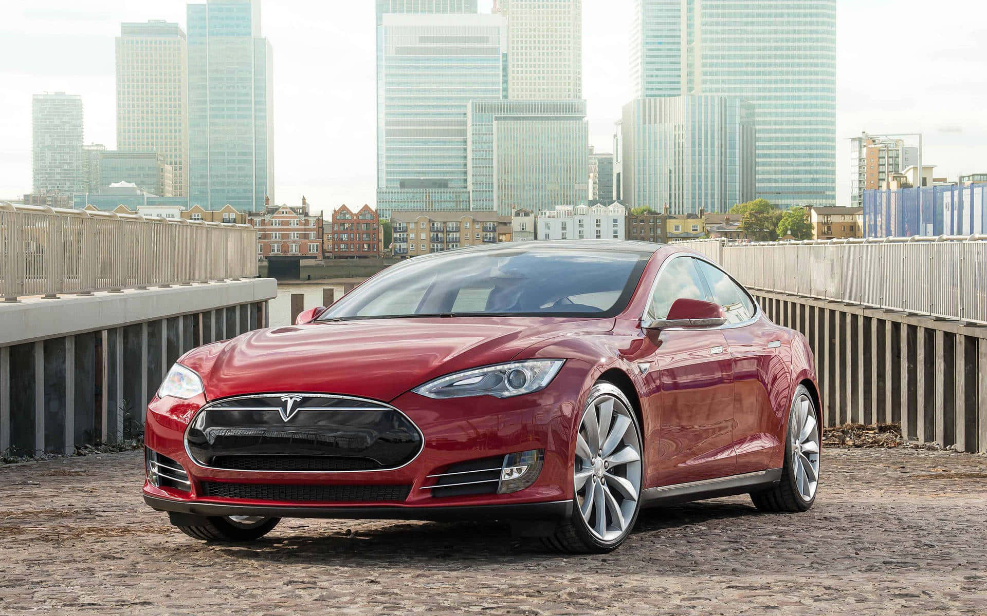 特斯拉 桌布 壁紙 — 一輛亮麗的紅色Tesla Model S停在鵝卵石橋上，背後是現代摩天大樓。