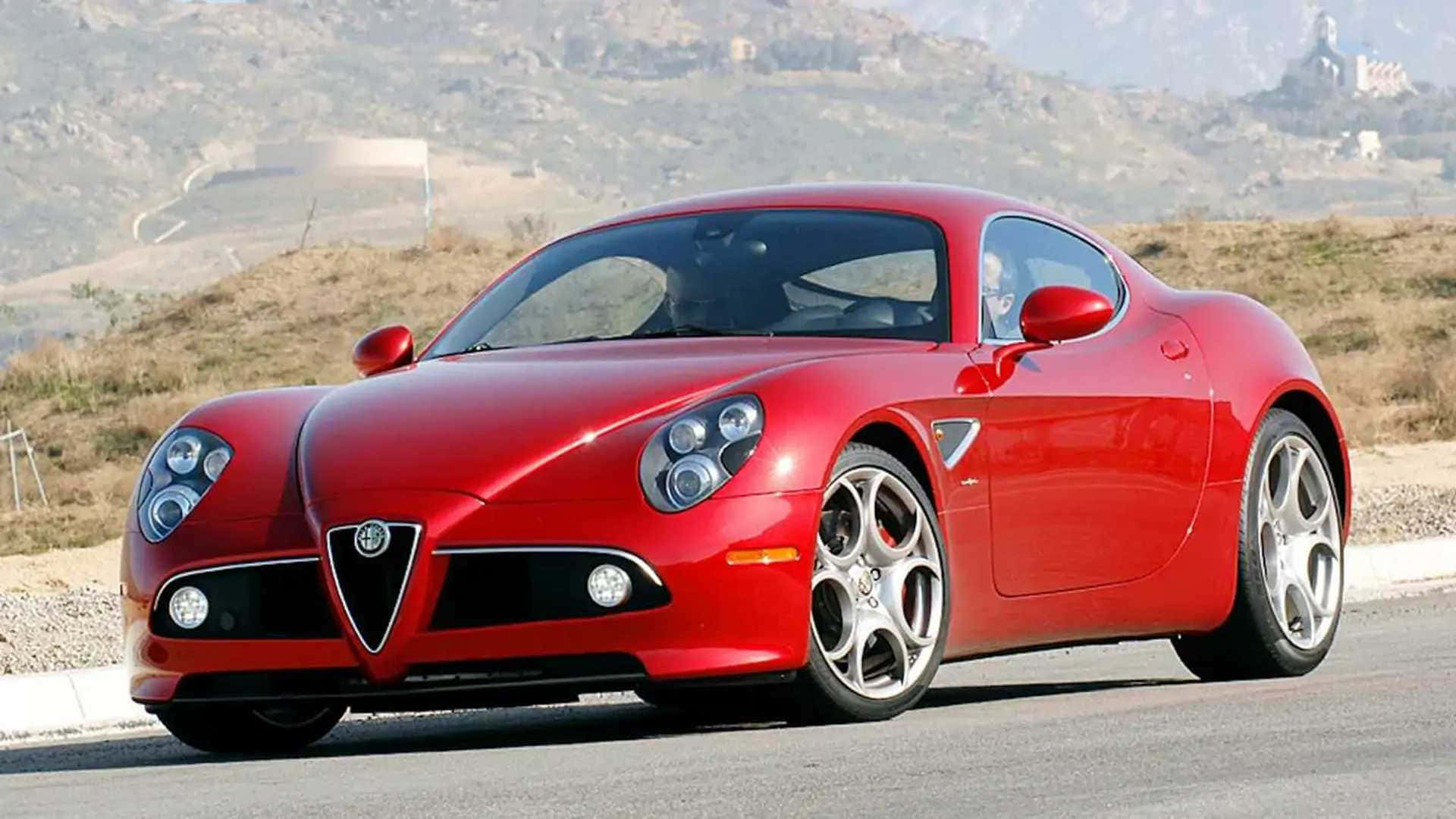 Alfa Romeo 8c Competizione 桌布 壁紙 — 一輛亮麗的紅色愛快羅密歐跑車停放在路邊，背景有乾燥的山丘和遠處的建築物。