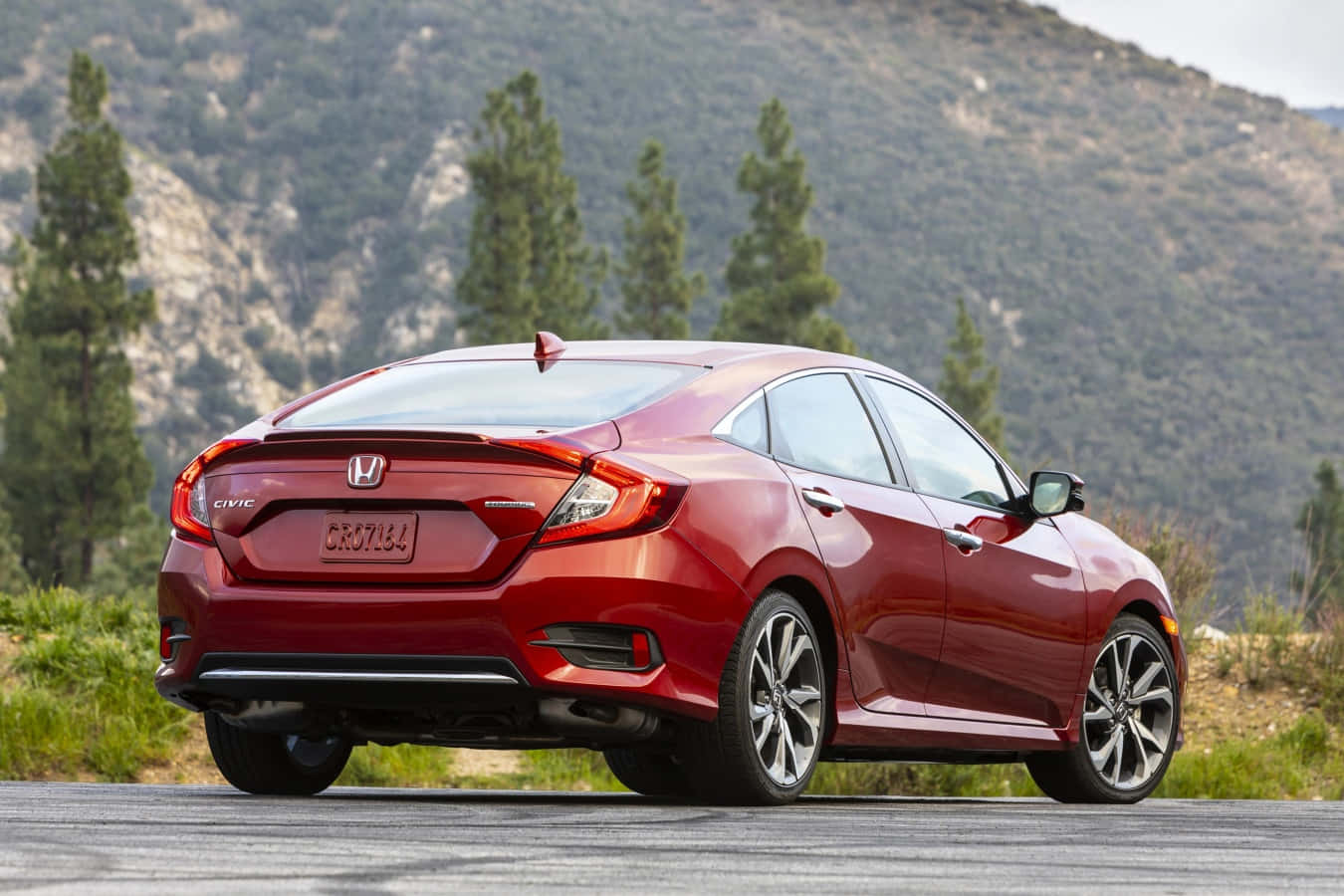 Honda Civic 桌布 壁紙 — 一輛亮麗的紅色本田思域房車停泊在鋪砌的道路上，背景有山脈和常綠樹。