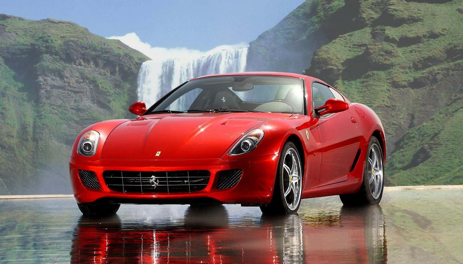 Ferrari 599 Gtb Fiorano 桌布 壁紙 — 一輛亮麗的紅色法拉利跑車在潮濕的道路上閃閃發光，背後是鬱鬱蔥蔥的群山和雄偉的瀑布。