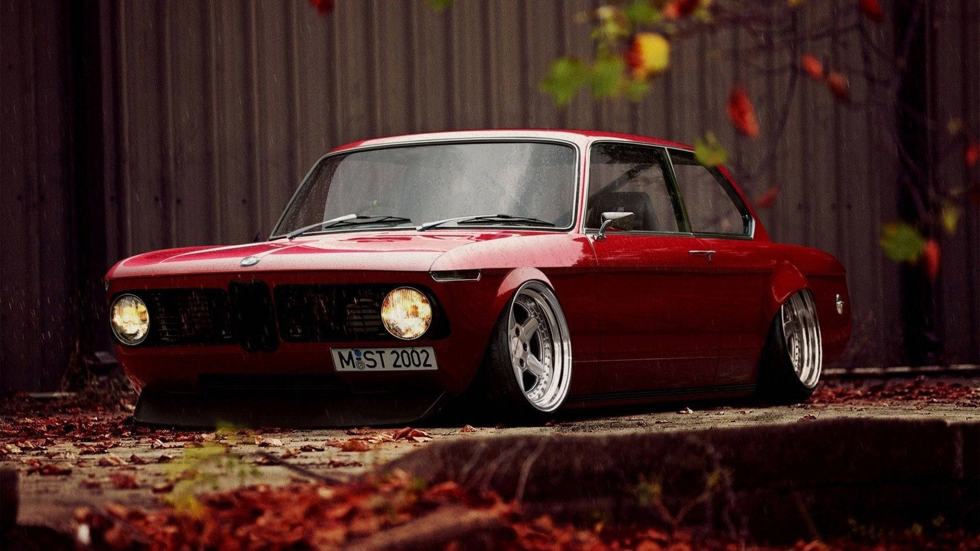 classic bmw 桌布 壁紙 — 一輛亮麗的紅色經典寶馬轎跑車，降低懸掛，停在石徑上，周圍有飄落的秋葉。