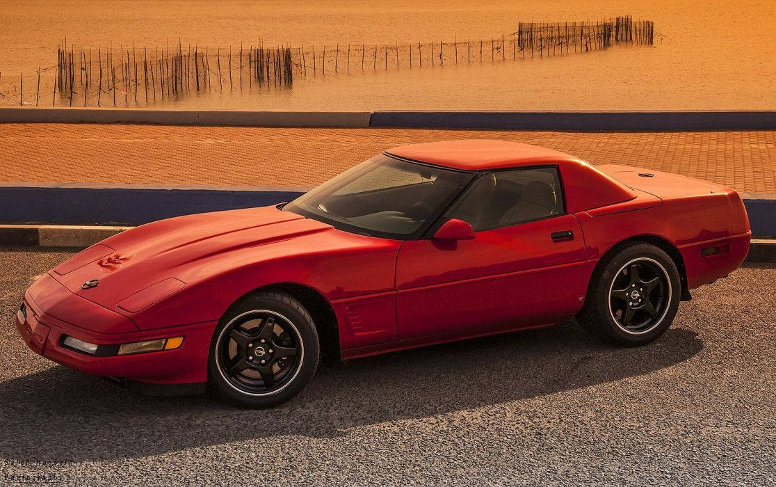 corvette 桌布 壁紙 — 一輛亮麗的紅色經典跑車停泊在沙灘旁的碎石上，正值黃金時刻。