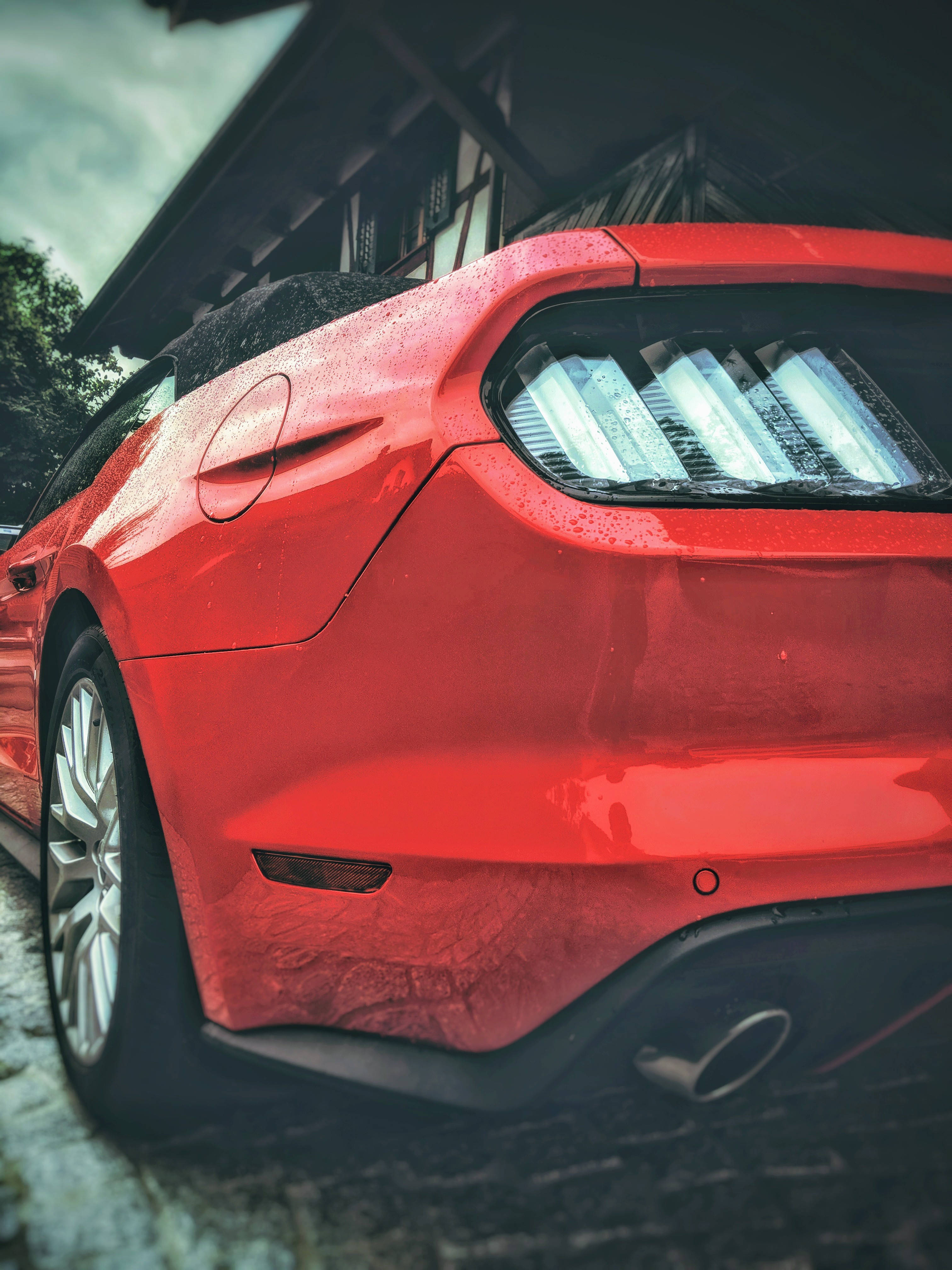 mustang HD 桌布 壁紙 — 一輛亮麗的紅色跑車，雨滴在陰天下一間木屋旁閃閃發光。