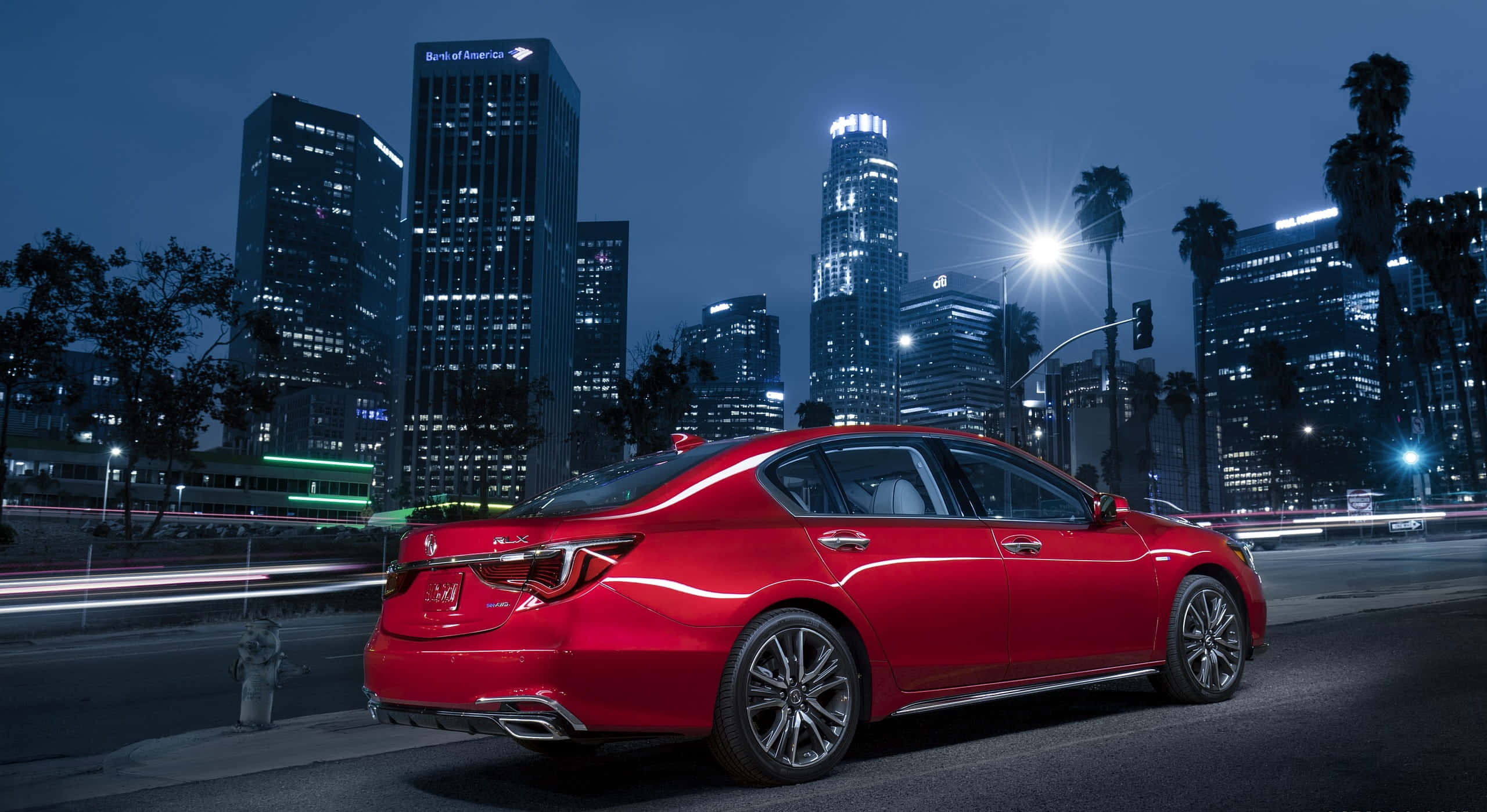 Acura Rlx 桌布 壁紙 — 一輛亮麗的紅色轎車在夜晚穿過霓虹燈閃爍的城市景觀，伴隨著流動的車流和背後閃耀的摩天大樓。