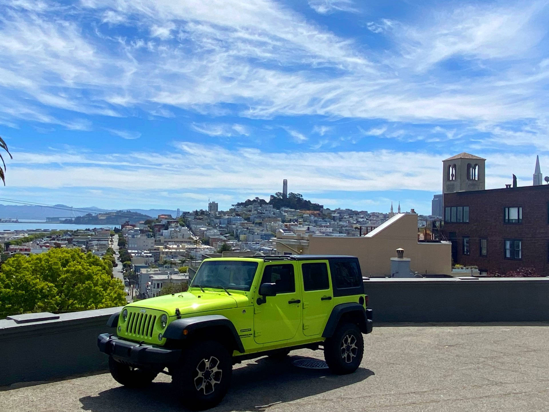 吉普 桌布 壁紙 — 一輛亮麗的青檸綠色Jeep Wrangler停泊在屋頂上，俯瞰著舊金山標誌性的城市景觀，在充滿活力的藍天下。