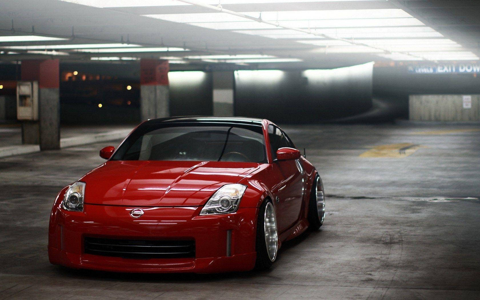 Nissan 350z 桌布 壁紙 — 一輛亮麗紅色日產350Z跑車，降低懸吊，戲劇性地停放在燈光昏暗的地下停車場。