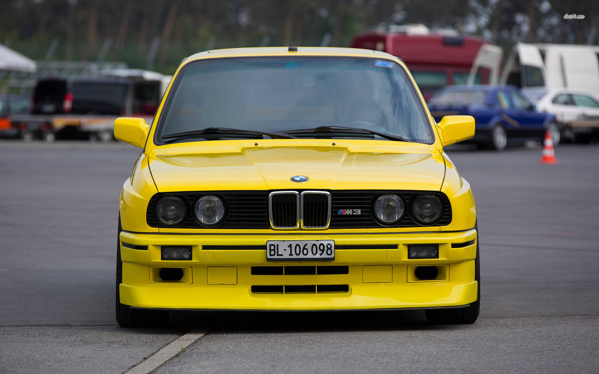 m 桌布 壁紙 — 一輛亮黃色BMW M3跑車在瀝青停車場面向前方，背景中其他車輛模糊不清。
