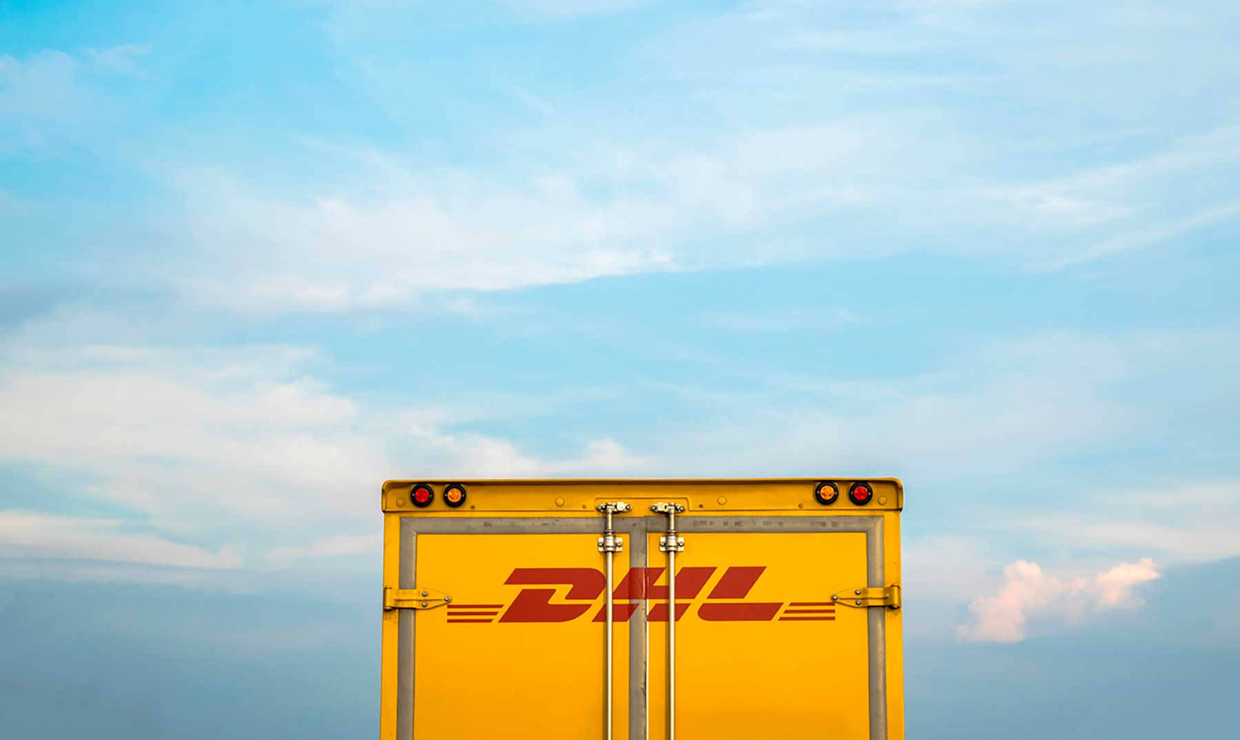 Dhl 桌布 壁紙 — 一輛亮黃色DHL送貨車的尾部，背景是柔和的藍天和縷縷白雲。