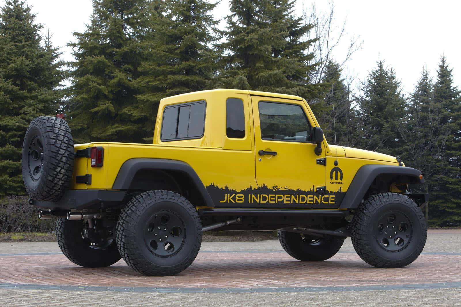 Jeep Gladiator 桌布 壁紙 — 一輛亮黃色升高底盤的Jeep Wrangler，帶有「JK8 INDEPENDENCE」貼紙，停在磚砌路面上，旁邊是常青樹。