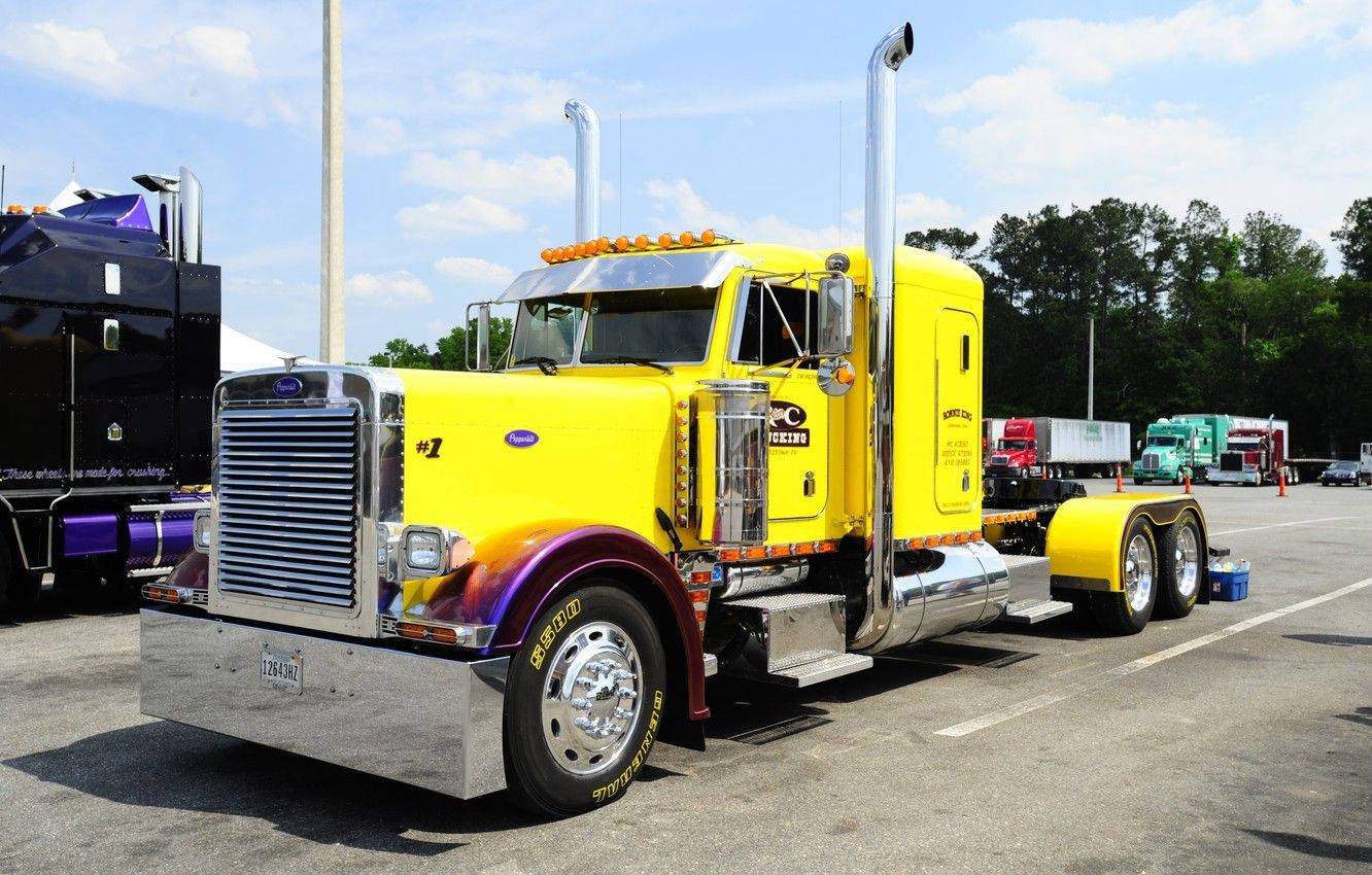 Trucks 桌布 壁紙 — 一輛亮黃色定制半掛卡車，帶有鍍鉻裝飾和彩虹塗裝車輪，停放在陽光明媚的場地。