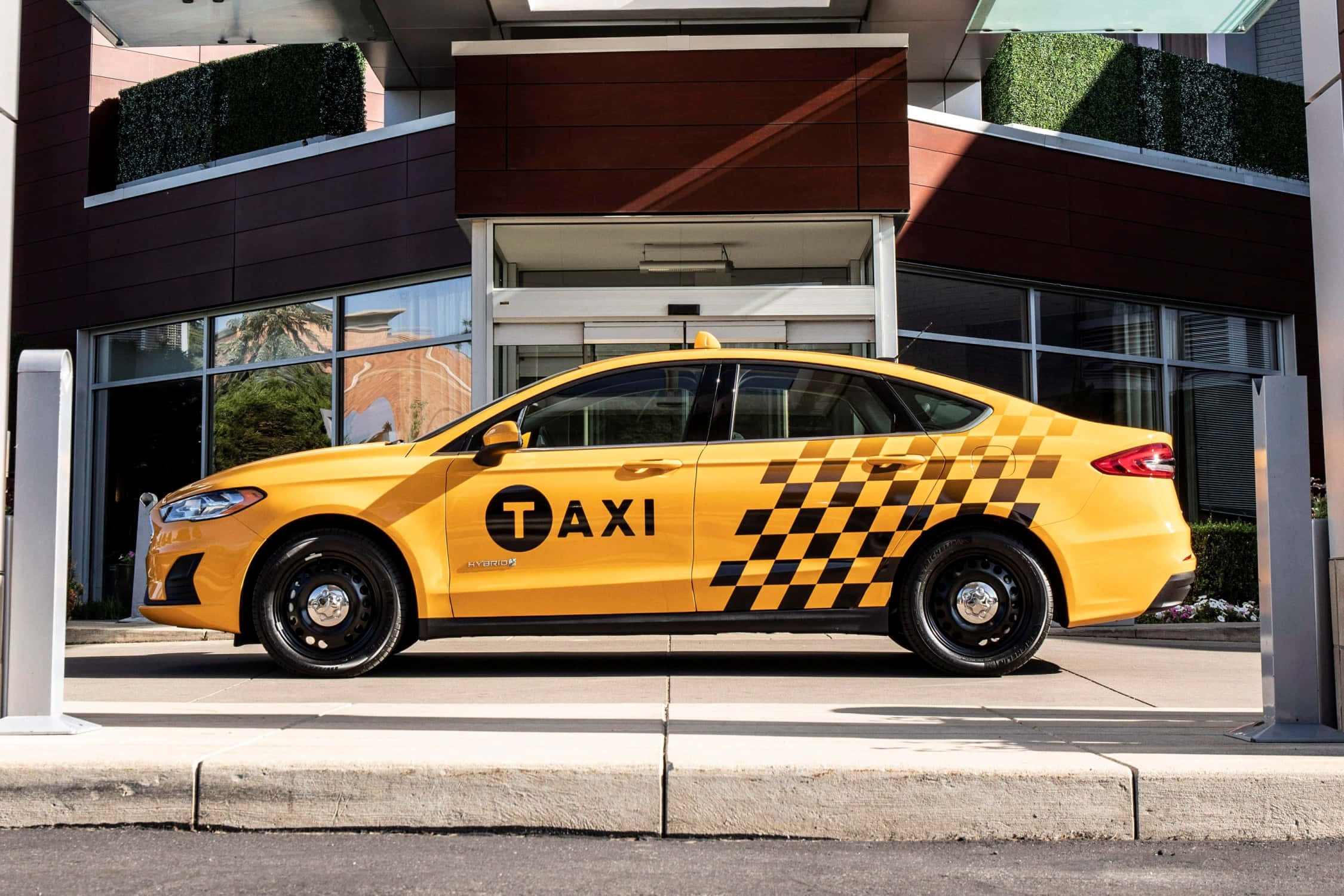 taxi 桌布 壁紙 — 一輛亮黃色帶黑色棋盤格圖案的計程車在陽光明媚的日子停在一棟現代建築外。