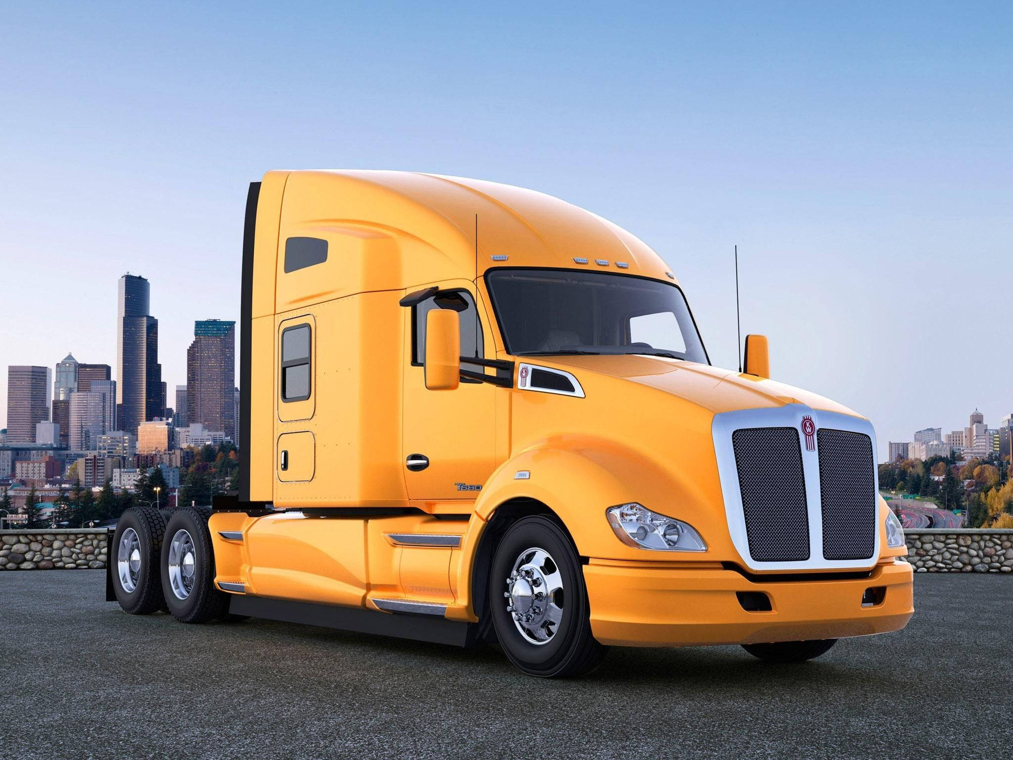 Kenworth 桌布 壁紙 — 一輛亮黃色的Kenworth半掛卡車停在鋪砌的觀景點上，背景是晴朗藍天下的現代城市天際線。