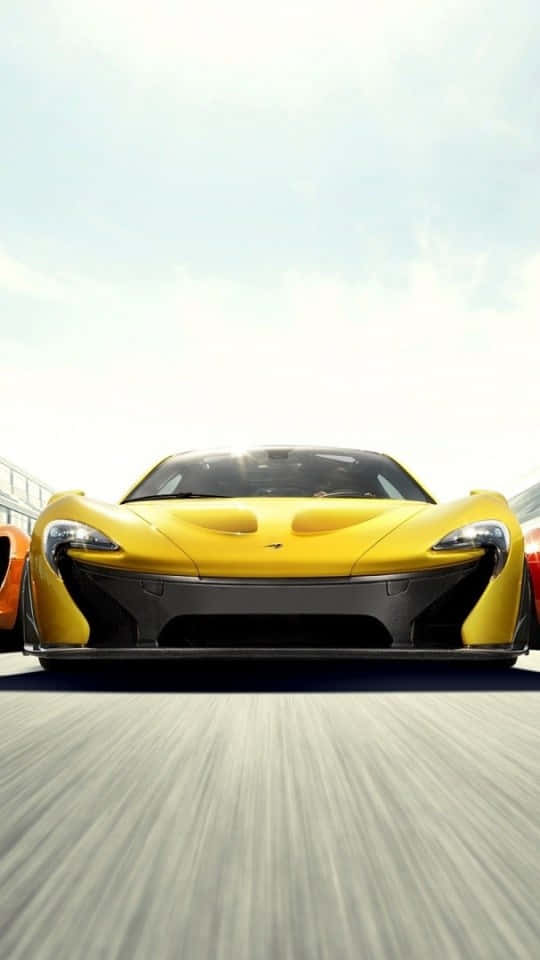 540x960 桌布 壁紙 — 一輛亮黃色的McLaren P1超級跑車在晴朗天空下，伴隨動態模糊效果在賽道上疾馳。