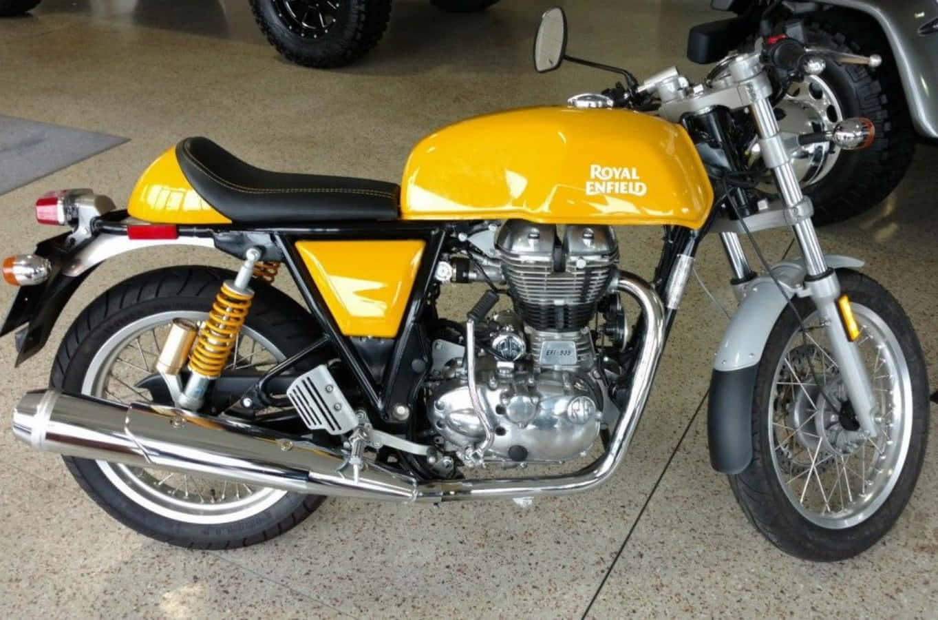 機車 桌布 壁紙 — 一輛亮黃色的Royal Enfield摩托車，帶有鍍鉻裝飾和黑色座椅，在室內斑點地板上展示。