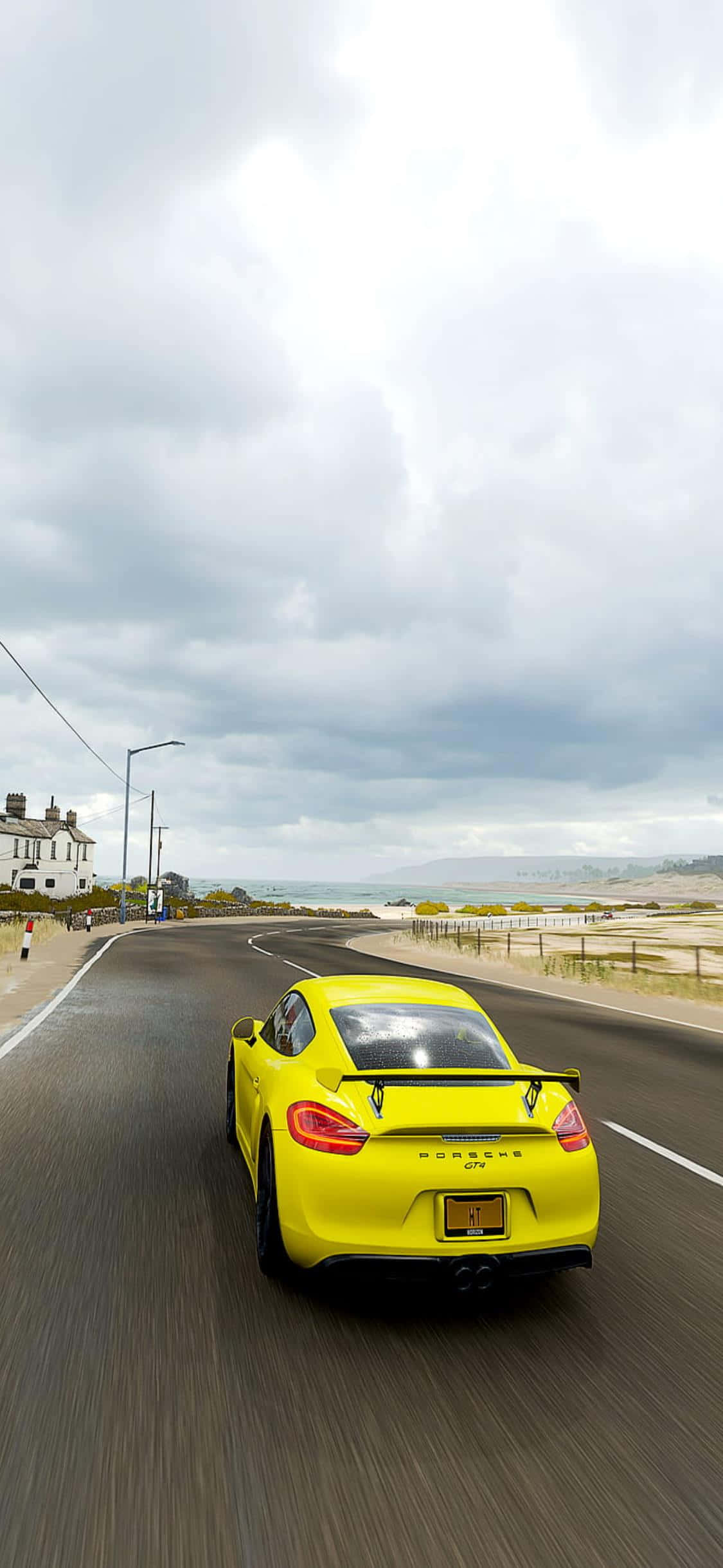 iPhone Xs Forza Horizon 4 桌布 壁紙 — 一輛亮黃色的保時捷Cayman在陰天沿著海岸公路飛馳，瀝青路面呈現動態模糊效果。