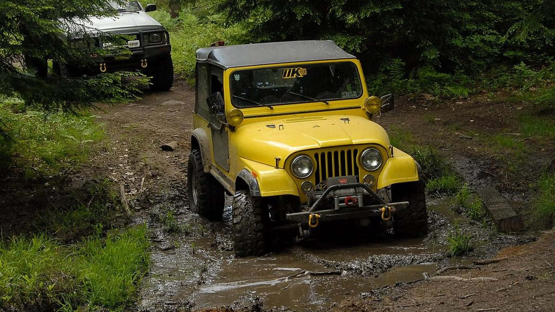 Jeep Cj 桌布 壁紙 — 一輛亮黃色的復古Jeep在泥濘的森林小徑上行駛，後面還有另一輛車。