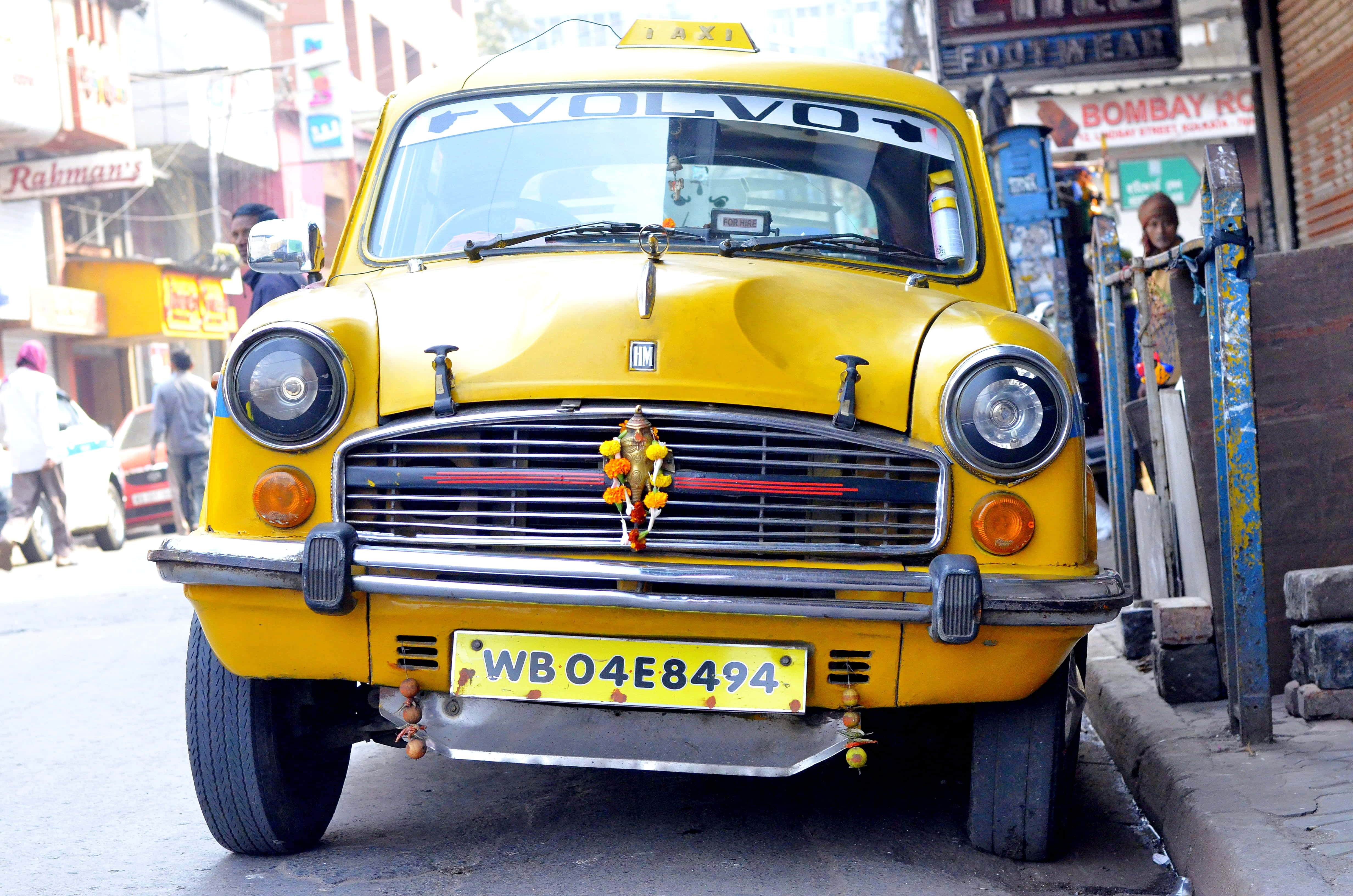 Yellow Cab 桌布 壁紙 — 一輛亮黃色的復古富豪計程車，飾以節日花環，停放在繁忙的印度街道上。
