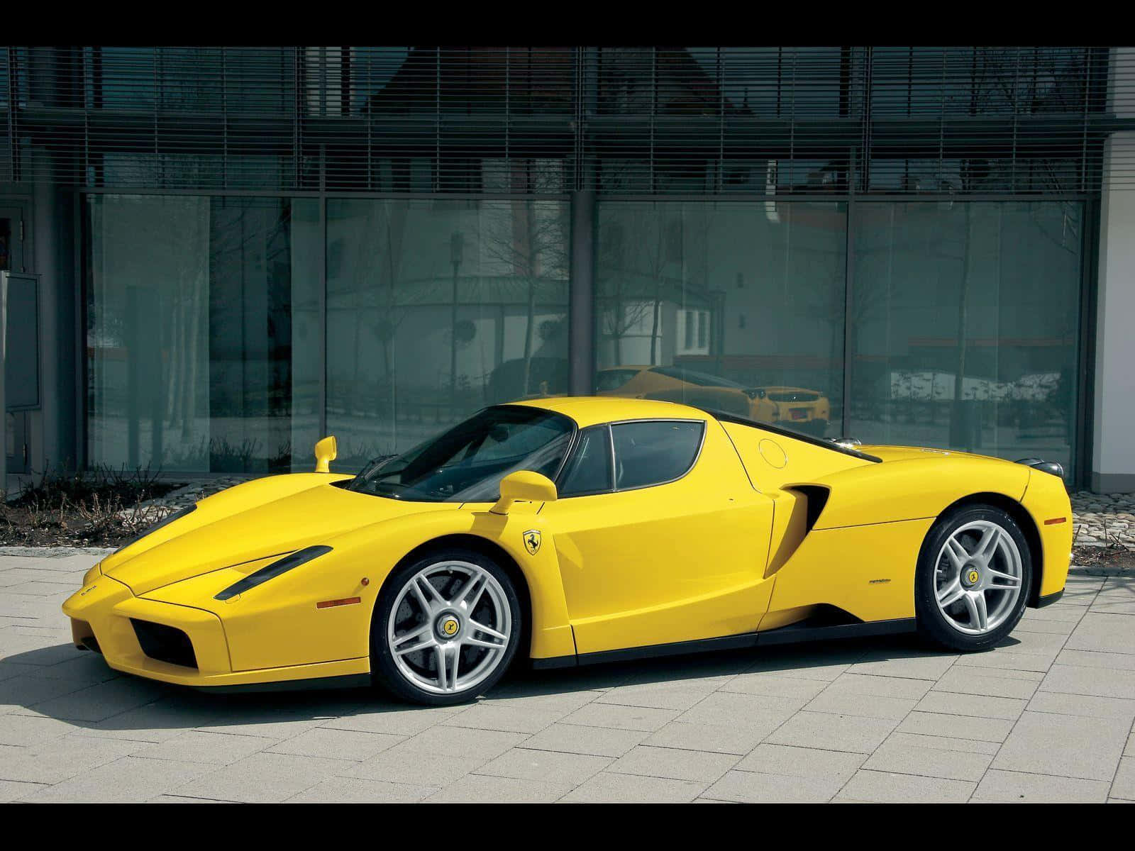 Ferrari Enzo 桌布 壁紙 — 一輛亮黃色的法拉利Enzo跑車停放在現代玻璃建築前的瓷磚廣場上。