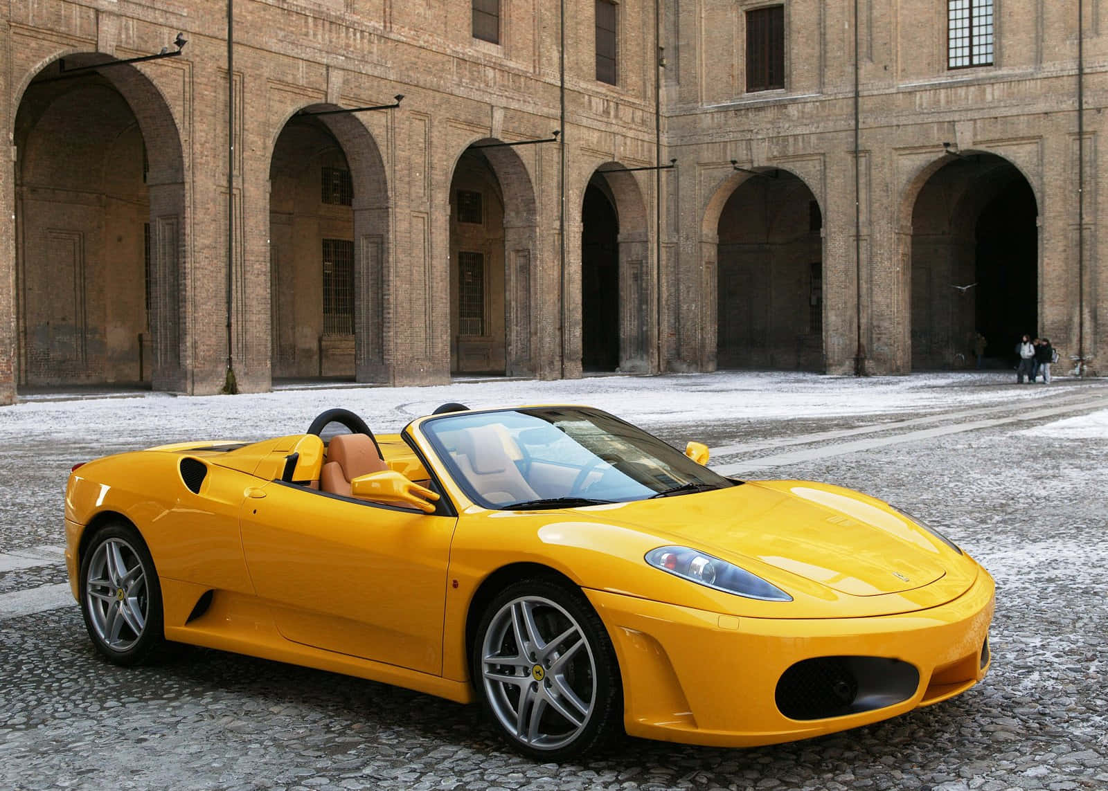 Ferrari F430 桌布 壁紙 — 一輛亮黃色的法拉利Spider停放在鵝卵石庭院前，面對一座宏偉的石拱廊建築。