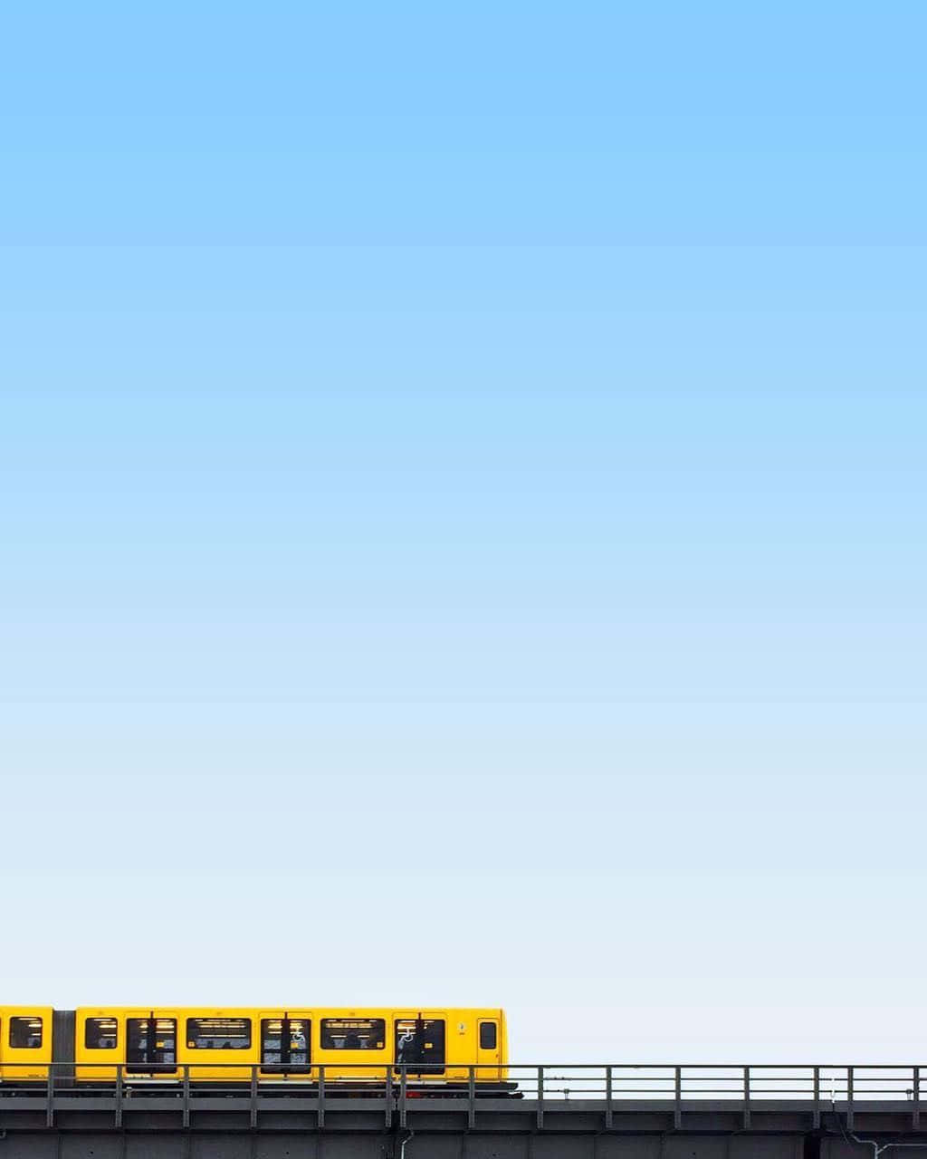 Minimalist Photography 桌布 壁紙 — 一輛亮黃色的火車在廣闊清澈的藍天下行駛在高架軌道上。