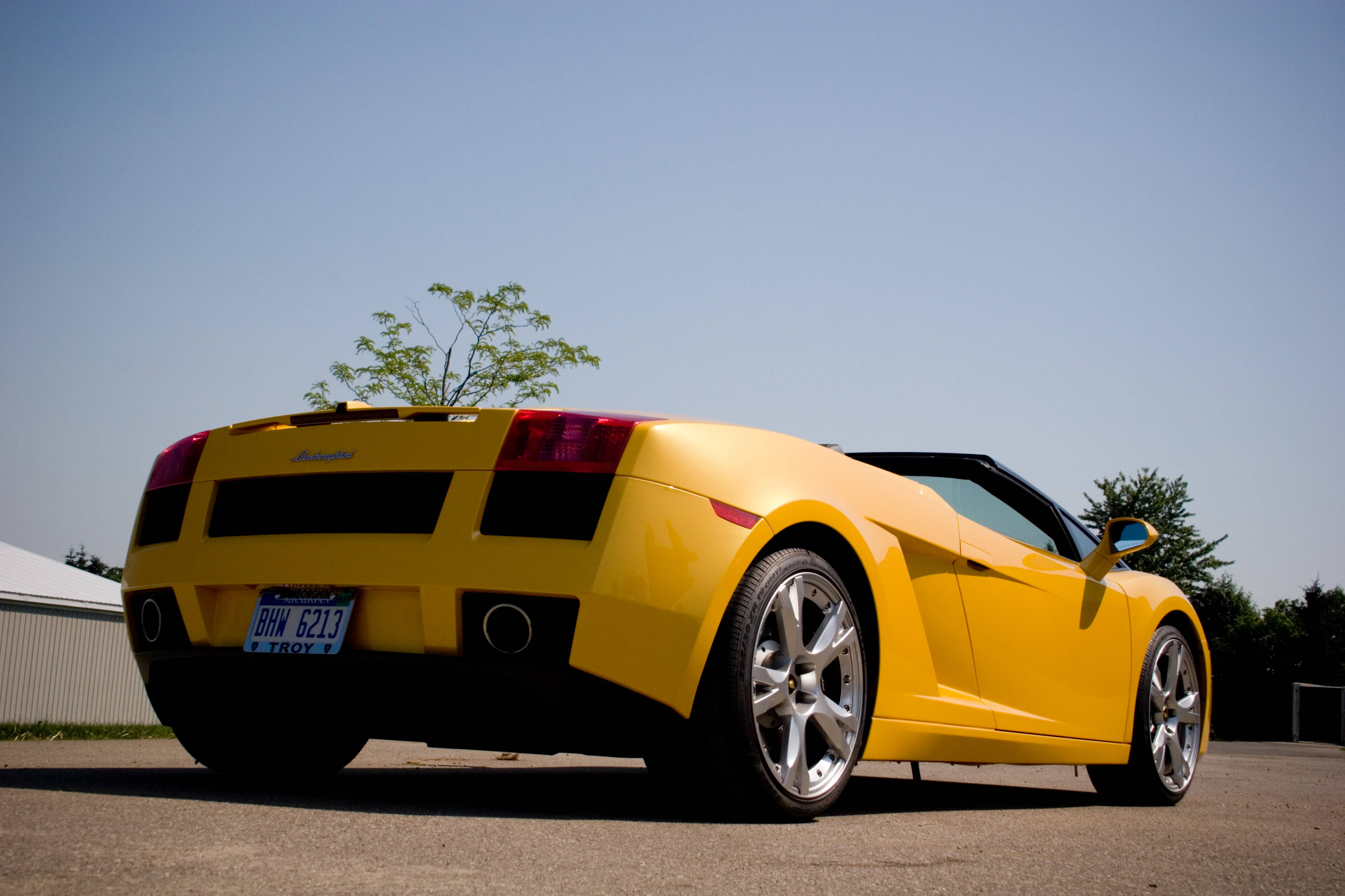 4K Lamborghini 桌布 壁紙 — 一輛亮黃色的藍寶堅尼 Gallardo Spyder 停泊在柏油路上，背景是晴朗的藍天和樹木。