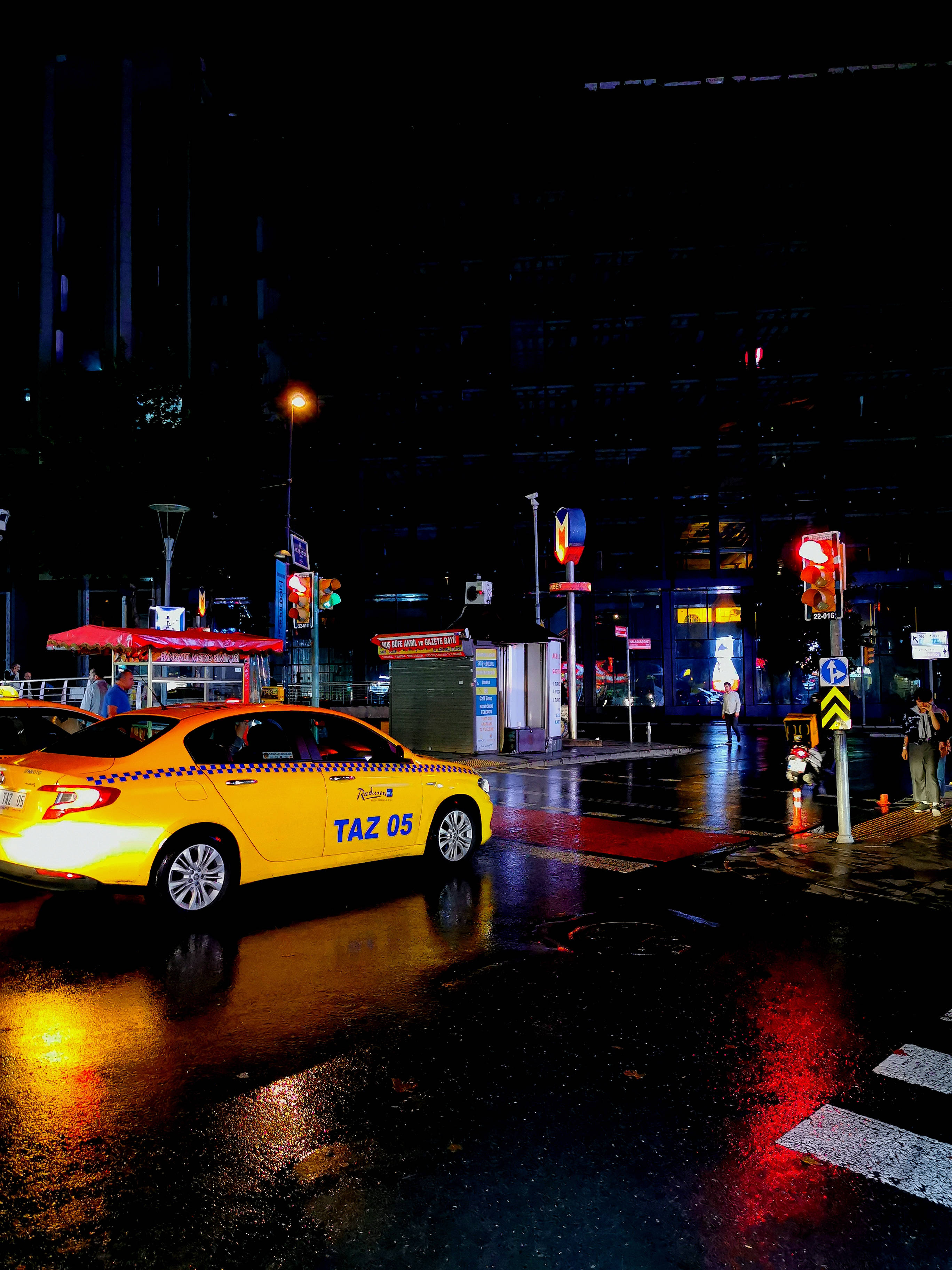 城市 桌布 壁紙 — 一輛亮黃色的計程車在夜間滑過被雨水浸濕的城市街道，其燈光在霓虹招牌下生動地反射在濕漉漉的路面上。