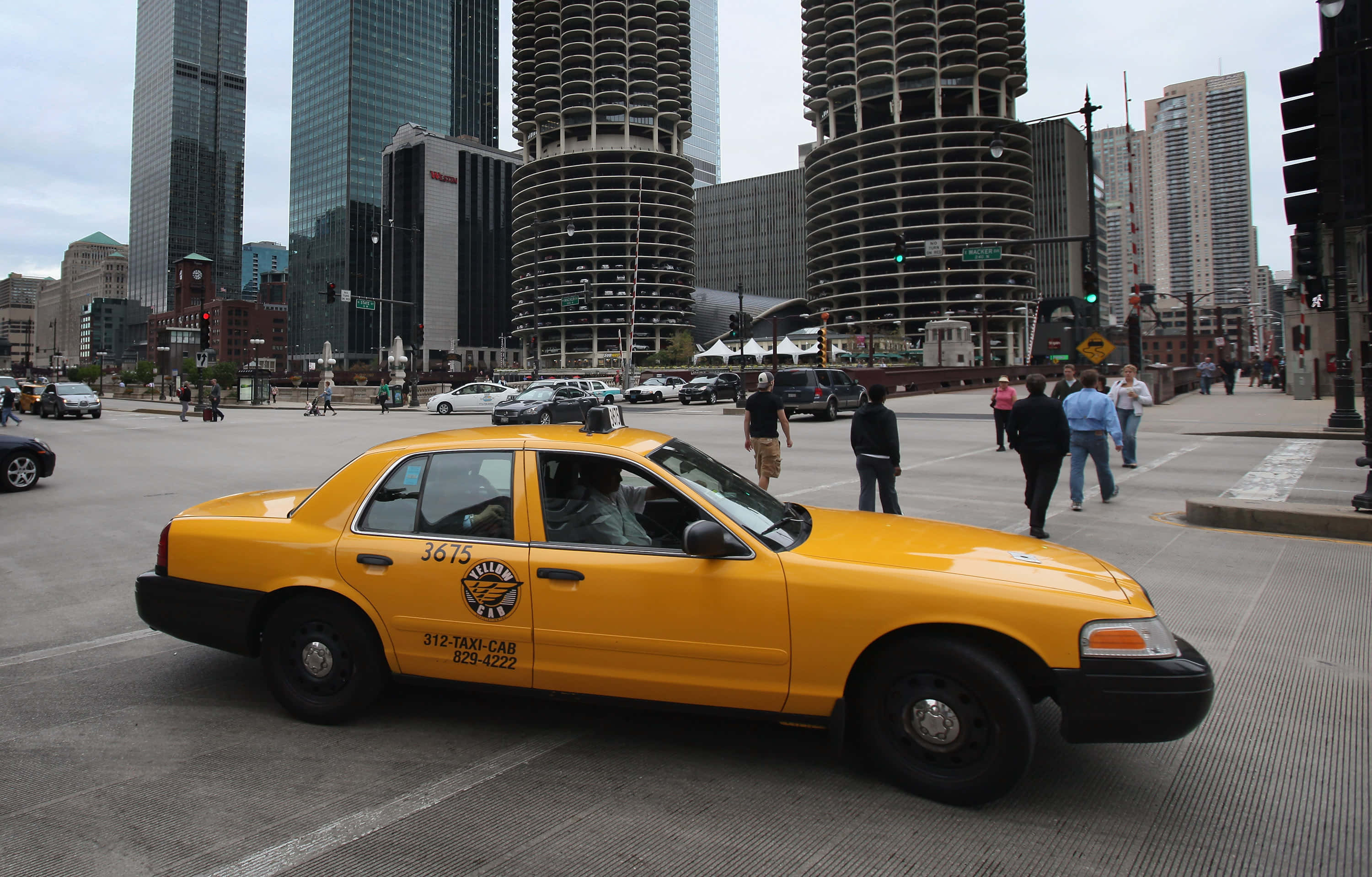taxi 桌布 壁紙 — 一輛亮黃色的計程車在繁華的城市街道上行駛，街道兩旁是高聳的摩天大樓和行人。