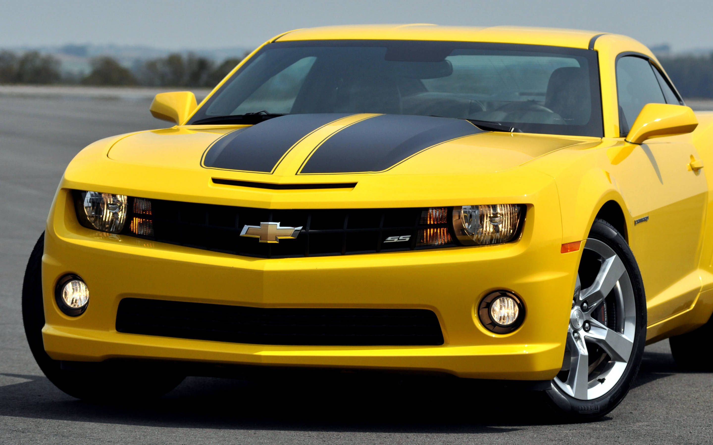 Chevrolet 桌布 壁紙 — 一輛亮黃色的雪佛蘭Camaro SS，帶有黑色賽車條紋，停在瀝青路面上，在晴朗的日光下。