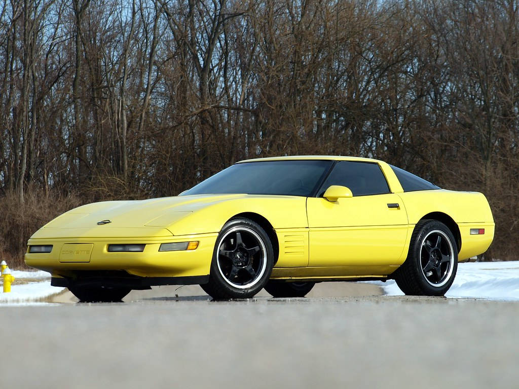 corvette 桌布 壁紙 — 一輛亮黃色的雪佛蘭克爾維特跑車停在積雪的路邊，背景是光禿禿的樹木。