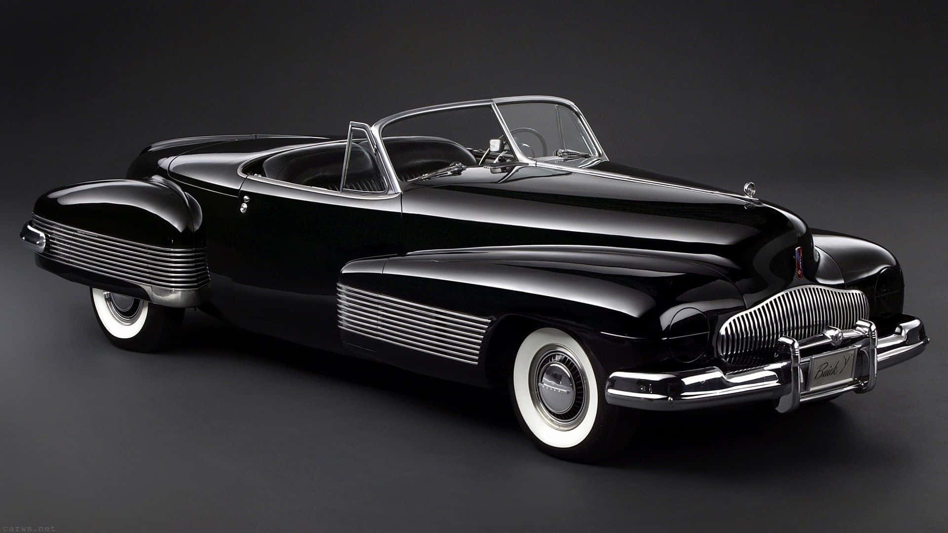 Black And White Vintage Car 桌布 壁紙 — 一輛亮黑色1940年代敞篷車，帶有鍍鉻裝飾和白色側壁輪胎，在深色工作室背景前擺放。