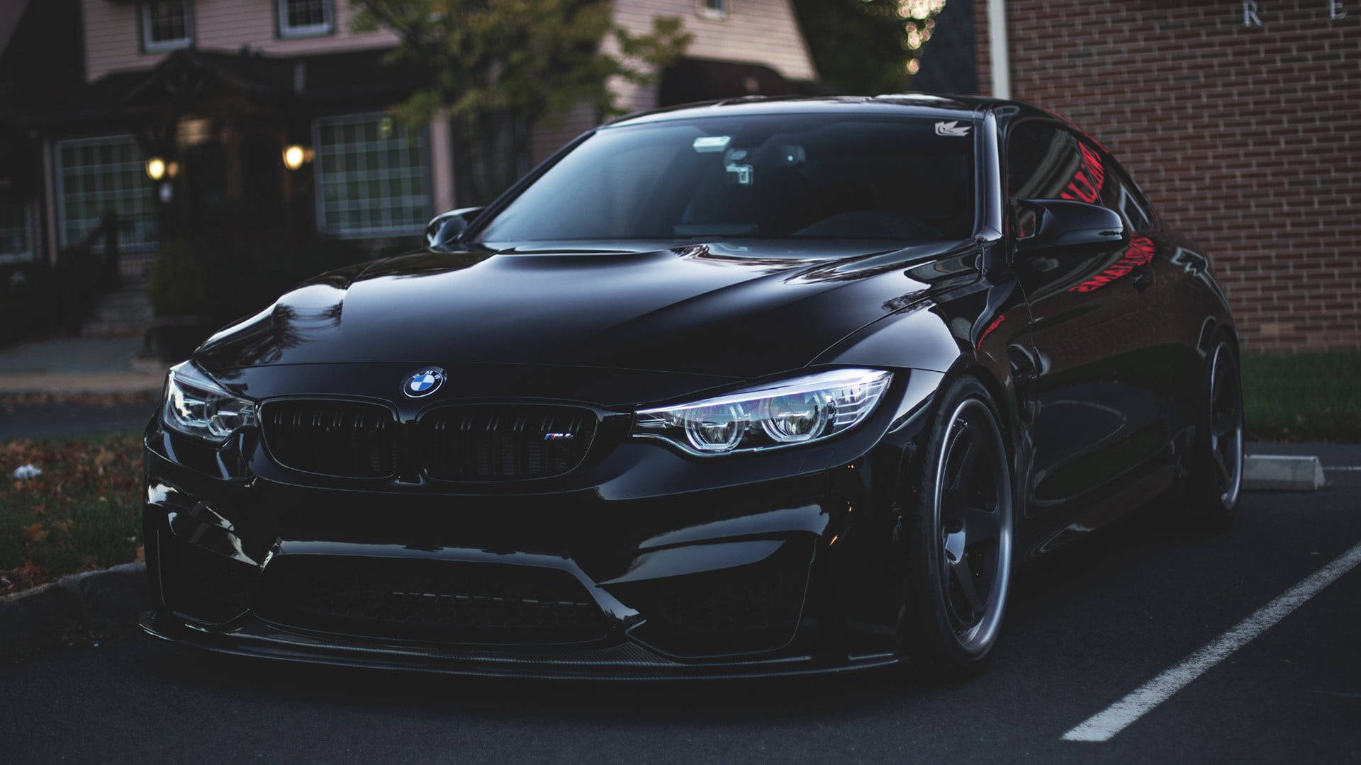 BMW 動圖 桌布 壁紙 — 一輛亮黑色BMW M4雙門跑車停放在住宅車道上，黃昏時分帶有溫暖的環境燈光。