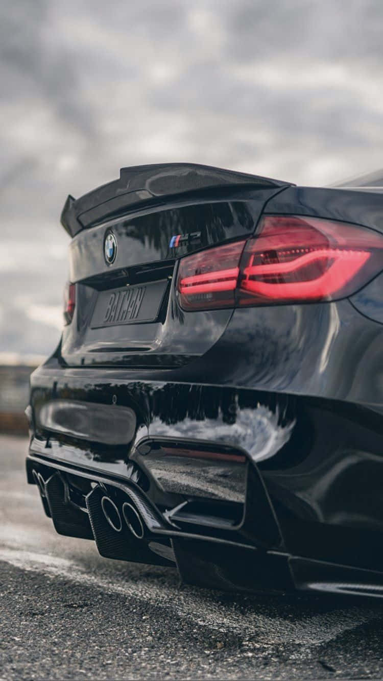 BMW 動圖 桌布 壁紙 — 一輛亮黑色BMW M5跑車，配備紅色尾燈和四出排氣管，停泊在潮濕的瀝青路上，天空多雲。
