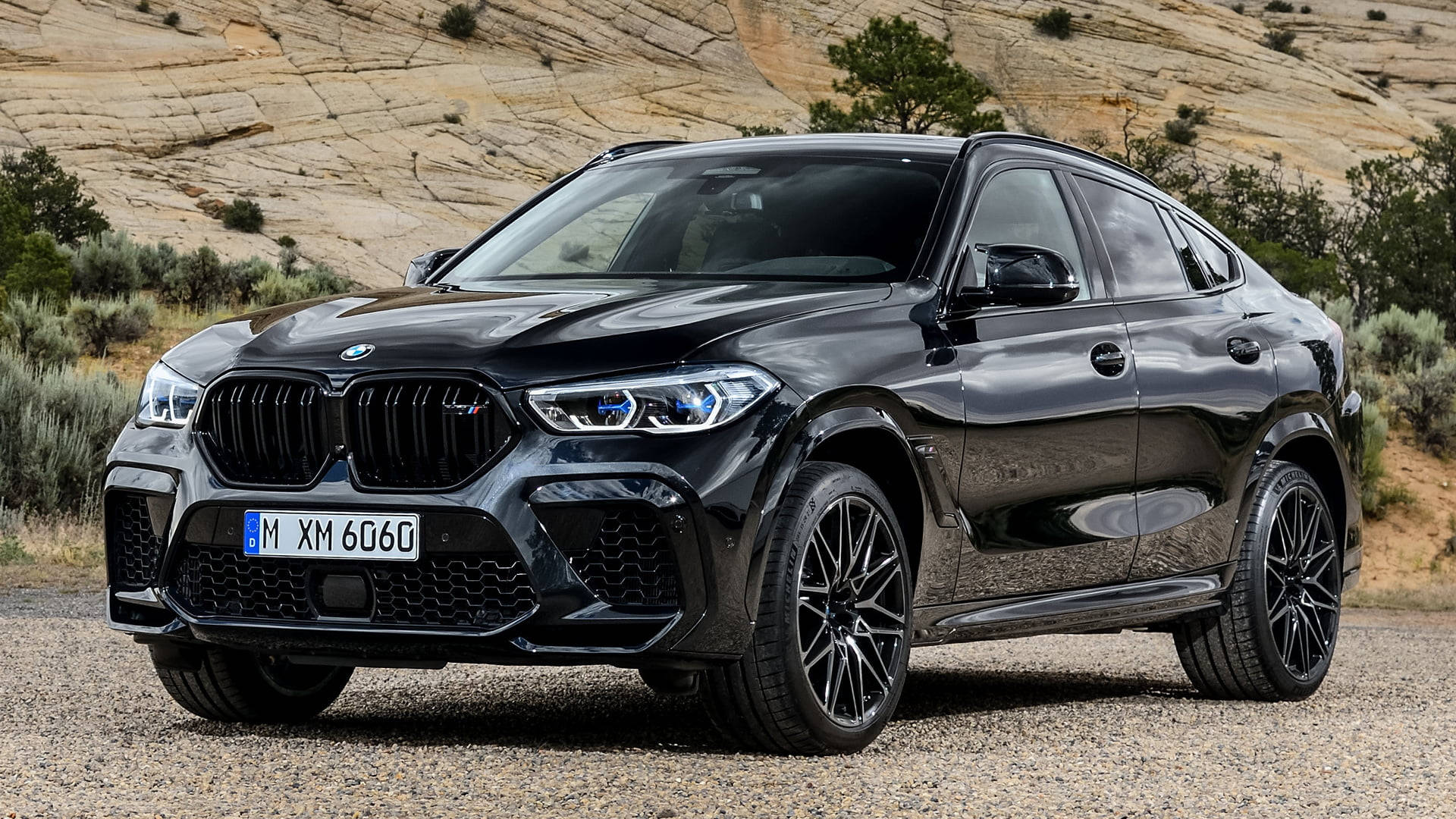 m 桌布 壁紙 — 一輛亮黑色BMW XM 6060 SUV停放在碎石上，背景是乾旱的山丘和稀疏的灌木。
