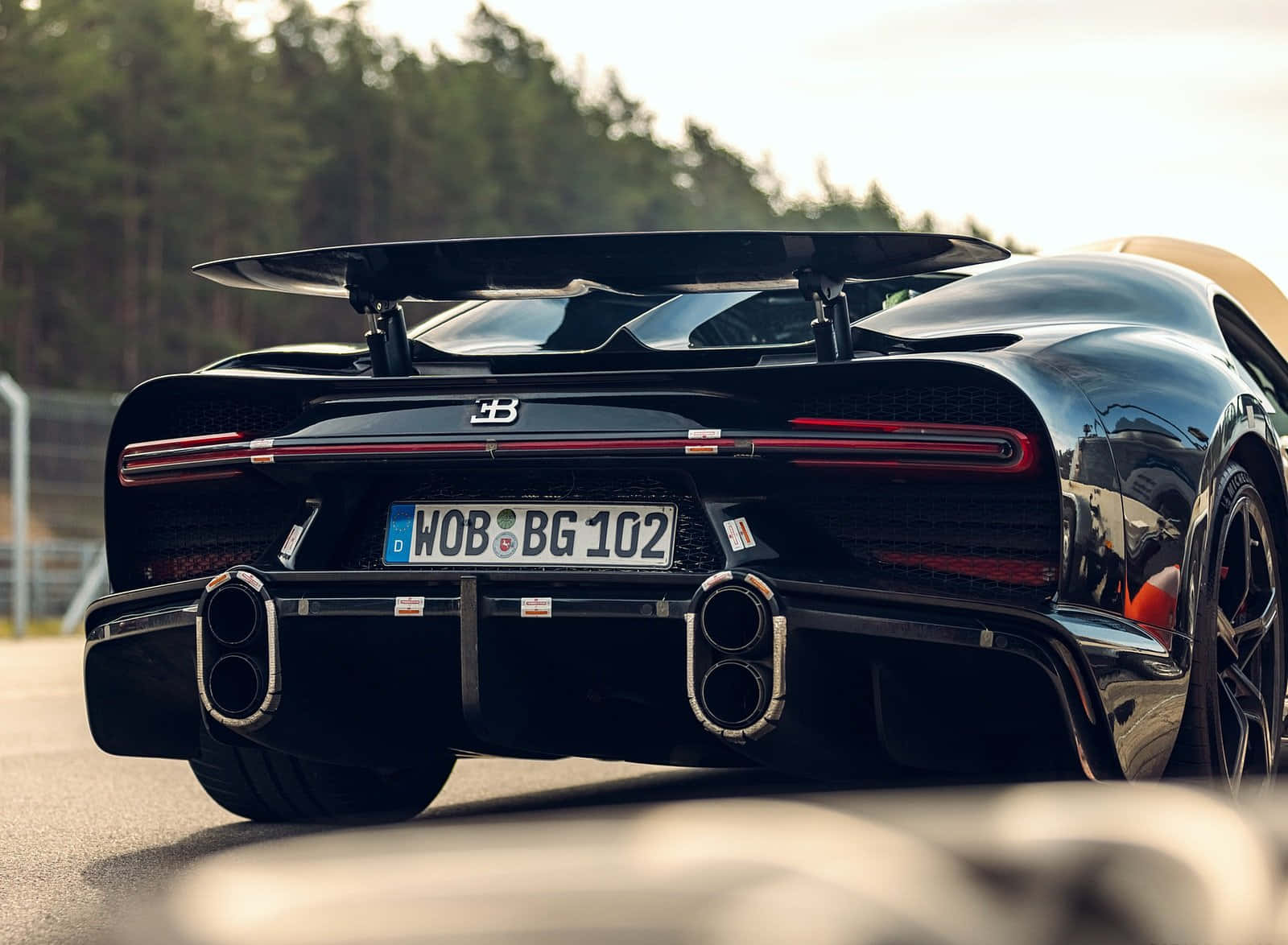 布加迪 桌布 壁紙 — 一輛亮黑色Bugatti Chiron Super Sport 300+停在賽道上，背景是森林和日落餘暉。