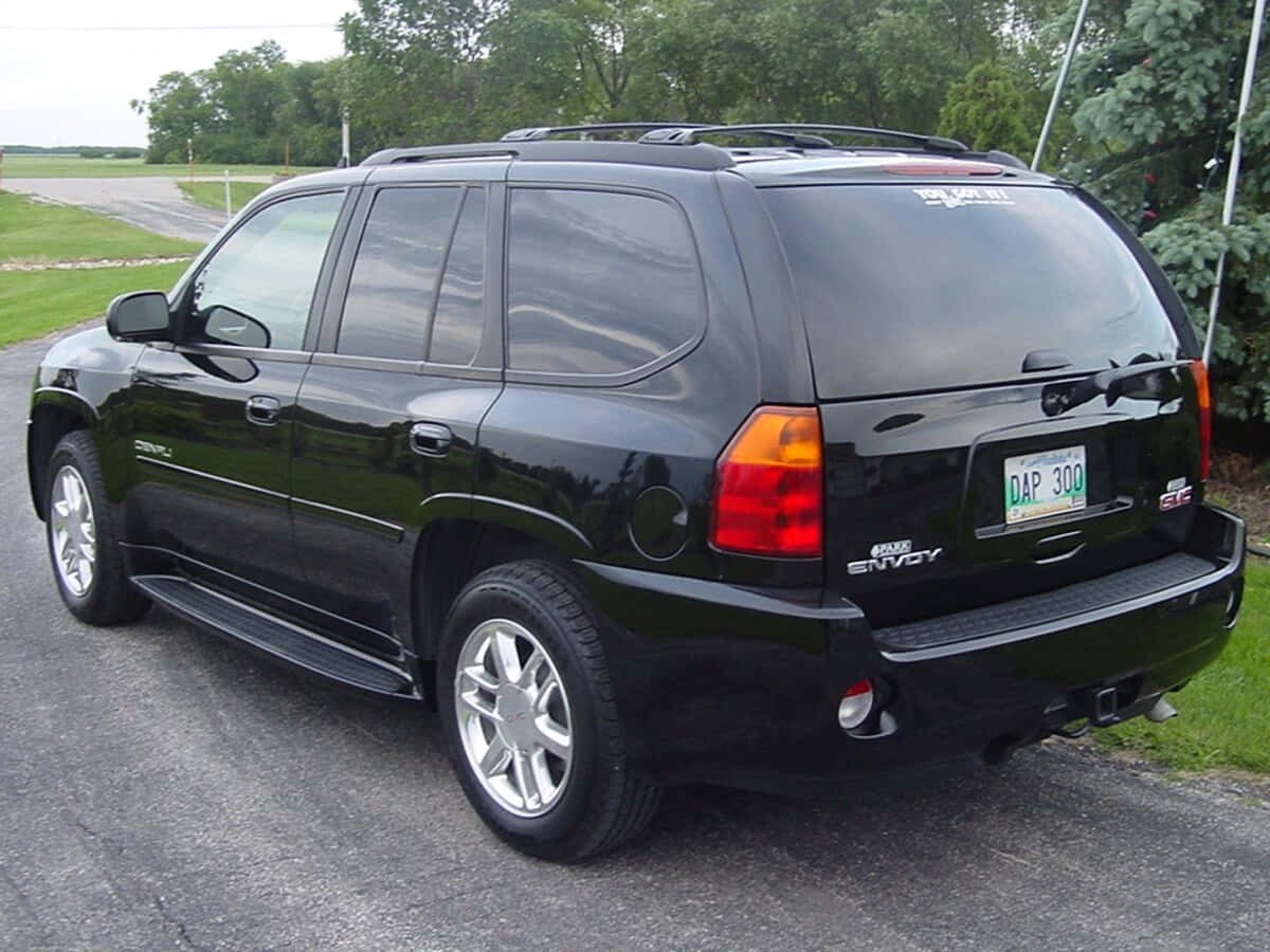 Gmc Envoy 桌布 壁紙 — 一輛亮黑色GMC Envoy SUV停放在柏油路上，背景有樹木和草地。