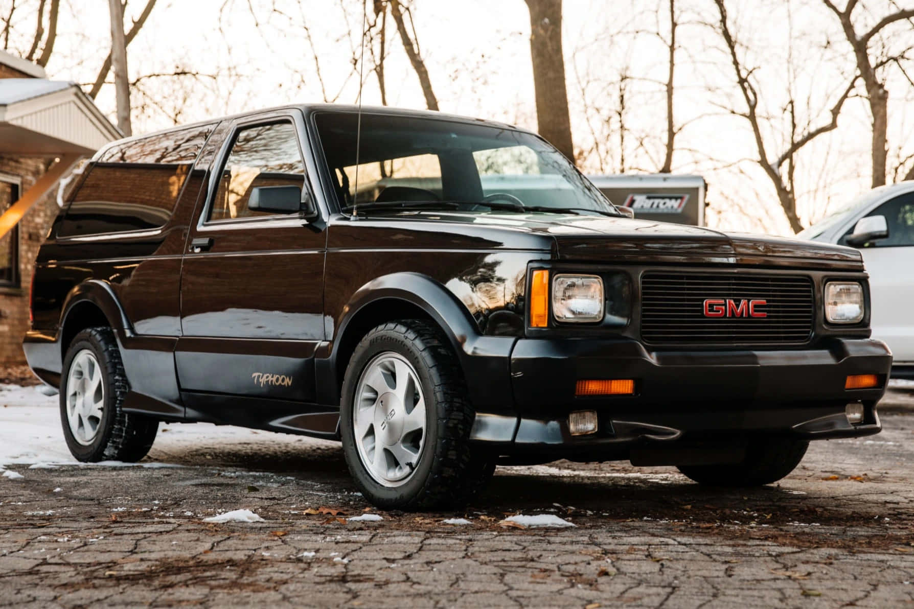 Gmc Typhoon 桌布 壁紙 — 一輛亮黑色GMC Typhoon皮卡車停在白雪覆蓋的鵝卵石車道上，背景是光禿禿的樹木。
