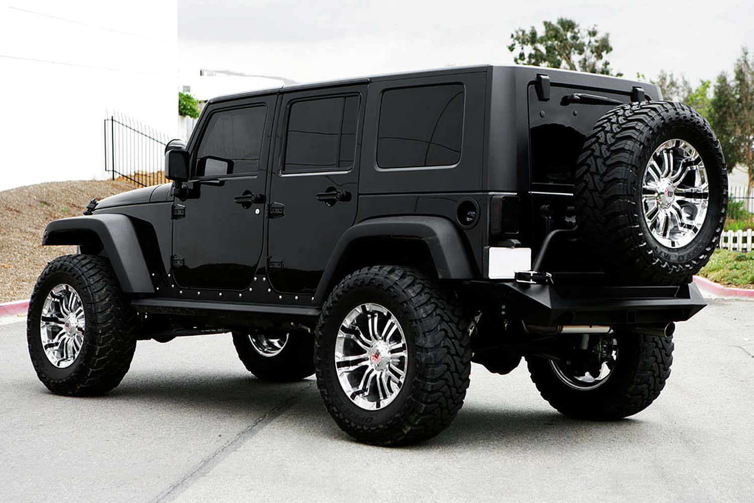 黑色吉普車 桌布 壁紙 — 一輛亮黑色Jeep Wrangler，配備鉻合金輪圈和超大輪胎，停在鋪砌的車道上。