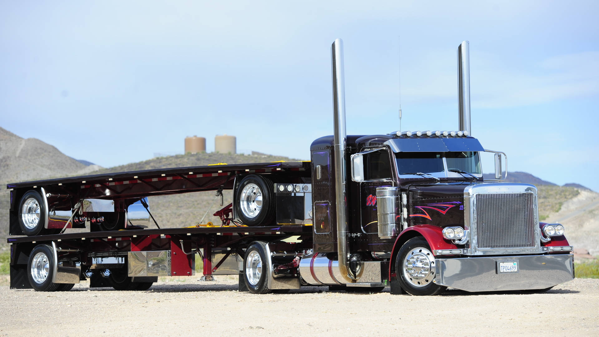 Peterbilt 桌布 壁紙 — 一輛亮黑色和紅色的半掛卡車，帶有鍍鉻裝飾和高排氣管，停在沙漠山丘附近的礫石上，天空清澈湛藍。