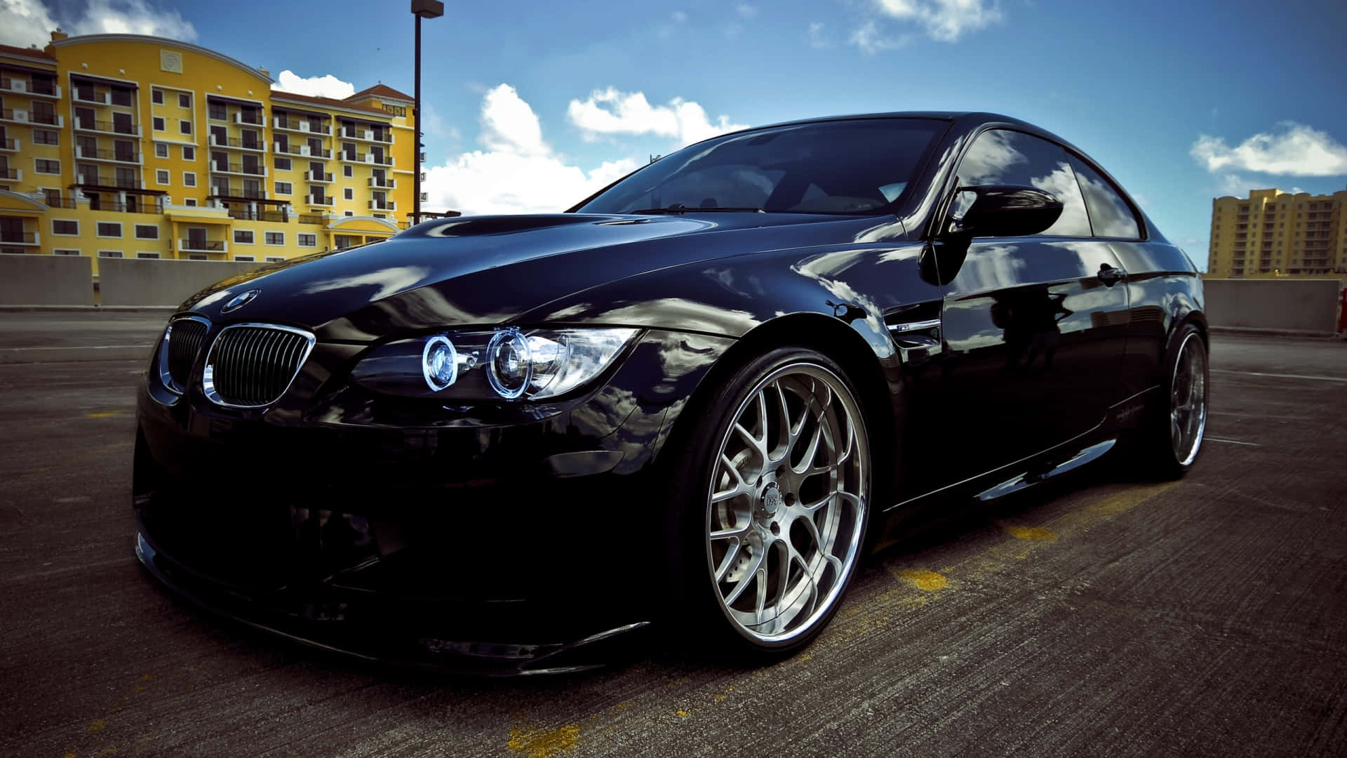 1920x1080 Bmw 桌布 壁紙 — 一輛亮黑色寶馬雙門轎跑車，配備定制銀色輪圈，停泊在屋頂上，天空湛藍，白雲點綴。