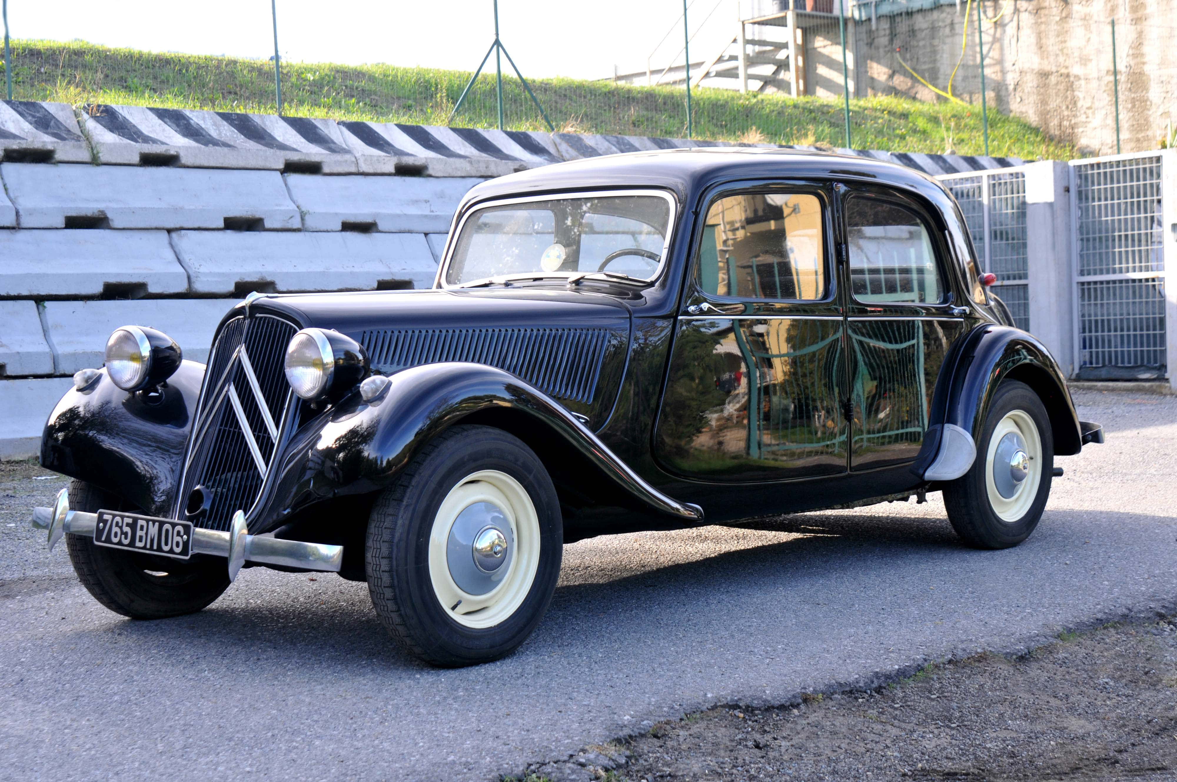 Citroen 桌布 壁紙 — 一輛亮黑色復古雪鐵龍2CV停泊在瀝青路上，旁邊是混凝土看台，在明亮的日光下。