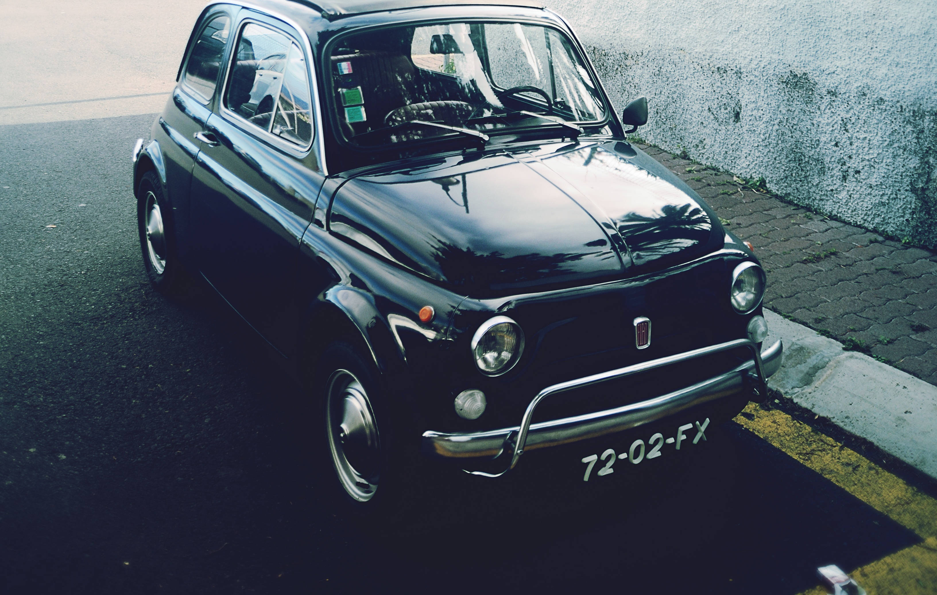 Fiat 桌布 壁紙 — 一輛亮黑色復古飛雅特500停泊在鵝卵石街道上，旁邊是紋理牆壁，在柔和日光下。