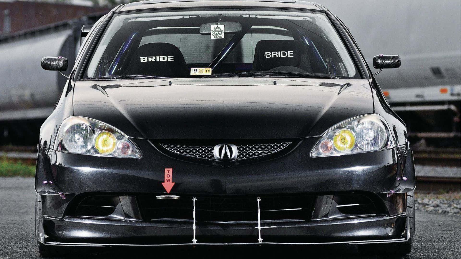 Rsx Type-s 桌布 壁紙 — 一輛亮黑色改裝Acura RSX跑車，配有黃色頭燈和Bride賽車座椅，停放在火車軌道附近。