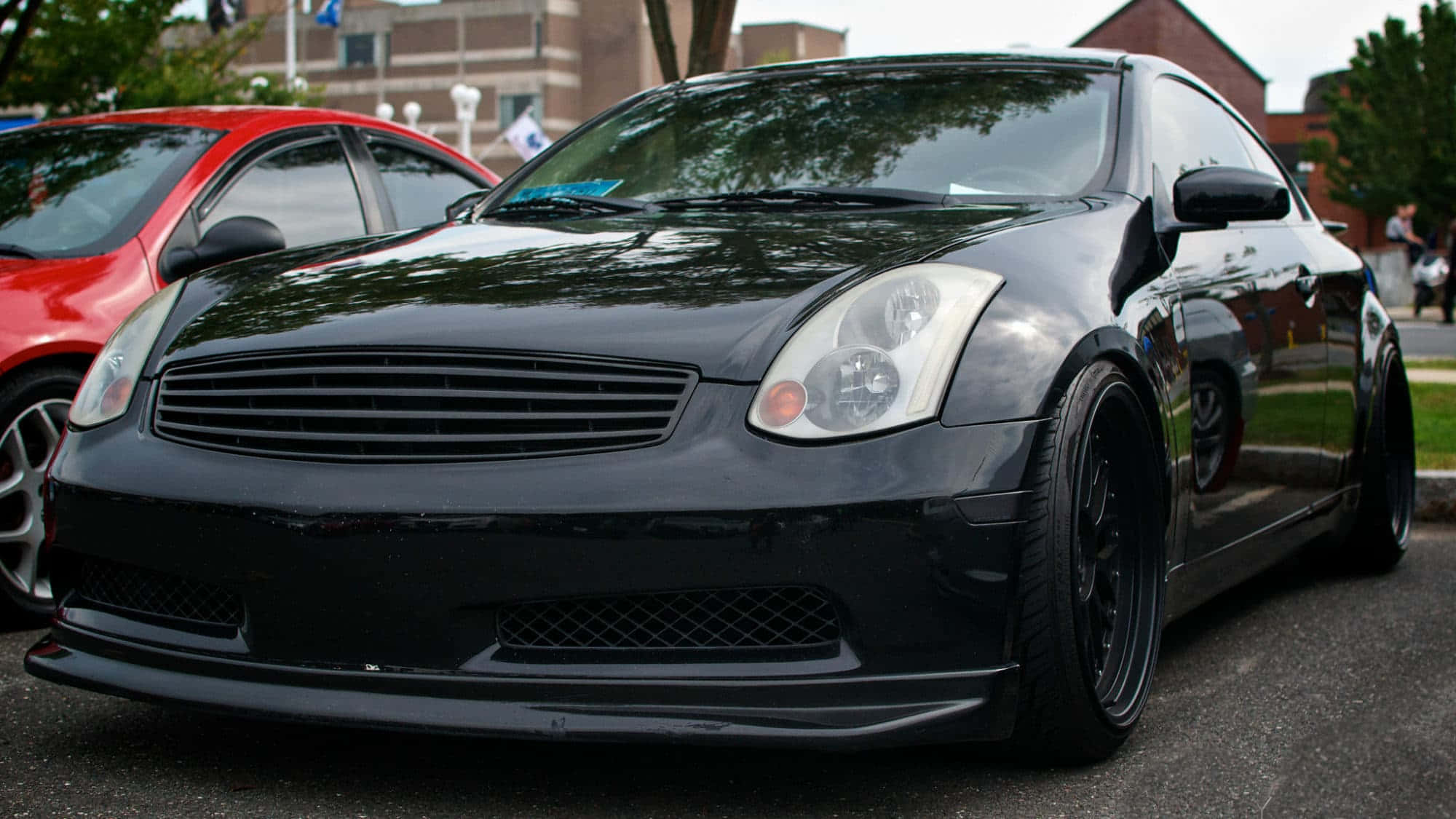 Infiniti G35 桌布 壁紙 — 一輛亮黑色改裝運動轎跑車停在柏油路上，旁邊有一輛紅色汽車，在日光下。
