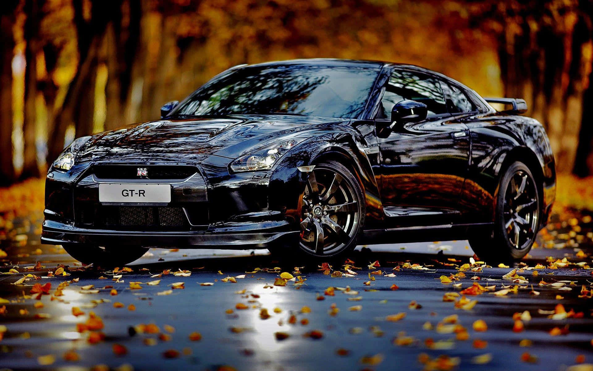 Gtr 桌布 壁紙 — 一輛亮黑色日產GT-R跑車停放在鋪滿金色秋葉的潮濕森林道路上。