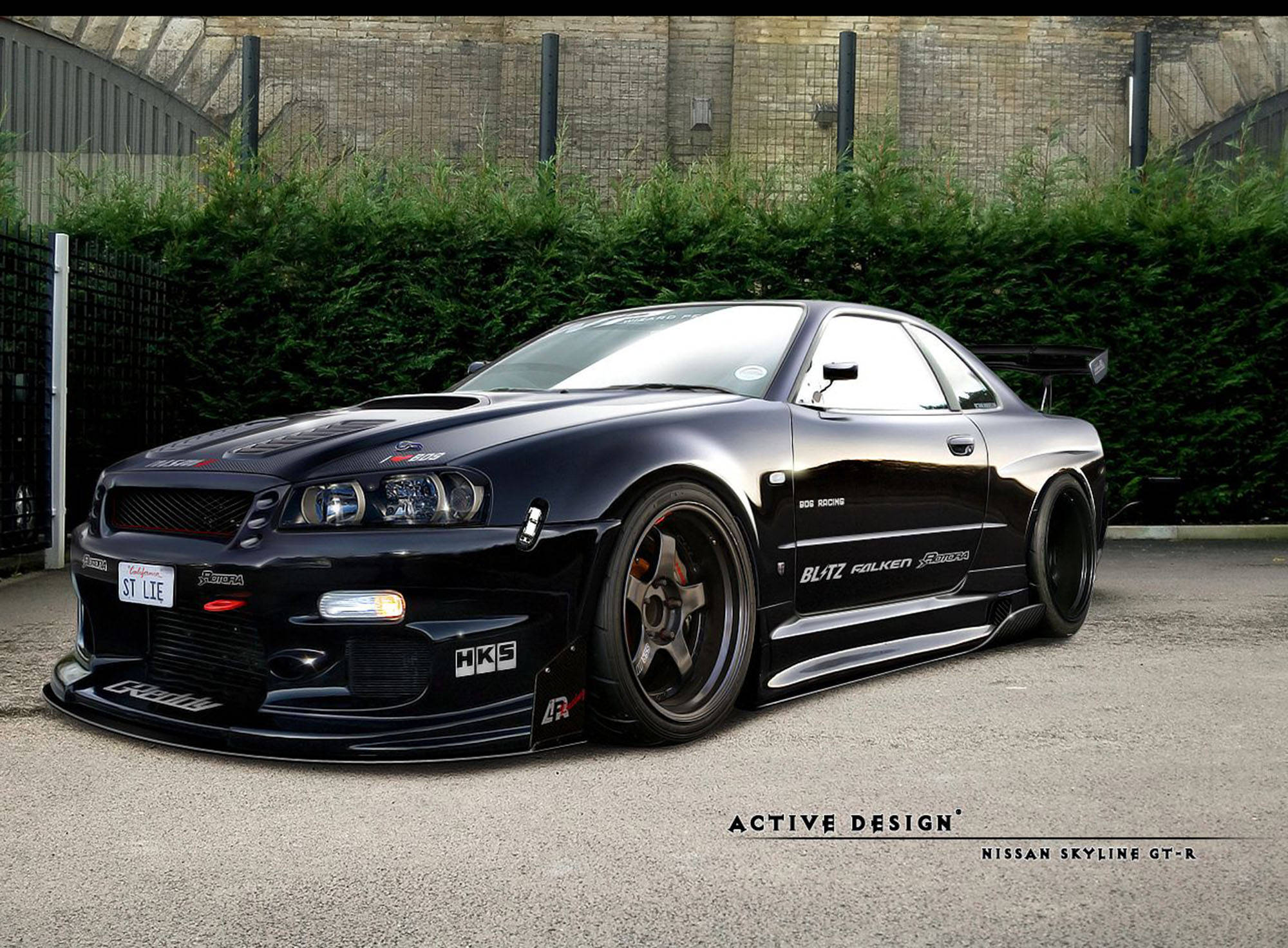 Gtr 桌布 壁紙 — 一輛亮黑色日產Skyline GT-R跑車，配備客製化寬體套件和賽車貼紙，停在柏油路上，旁邊有綠色樹籬。