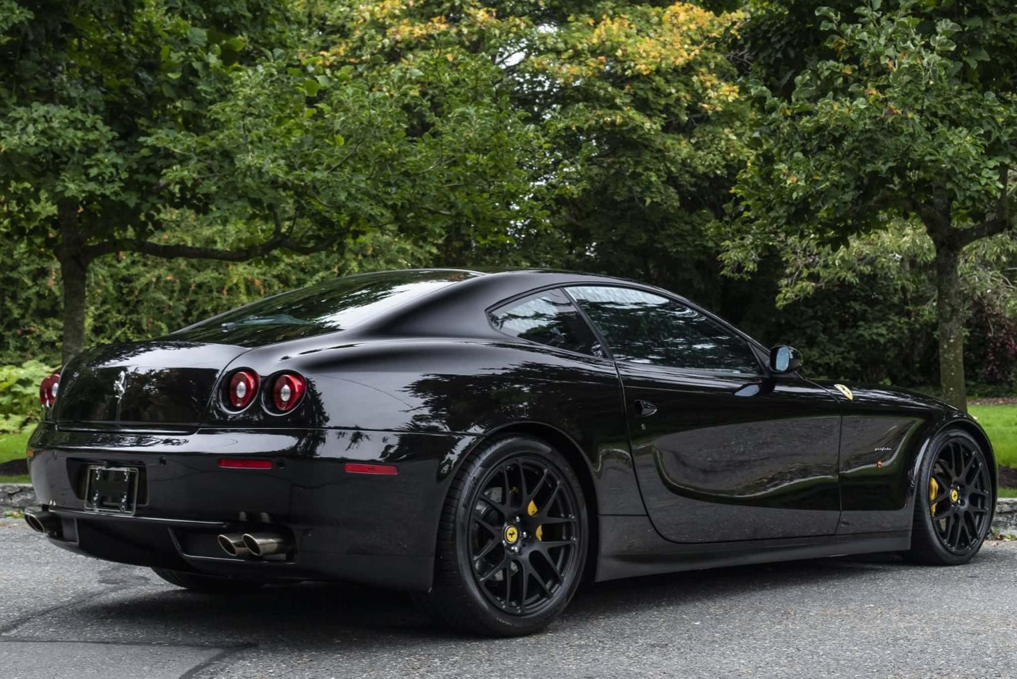 Ferrari 612 Scaglietti 桌布 壁紙 — 一輛亮黑色法拉利612 Superamerica停在柏油路上，背景是茂密的綠樹。