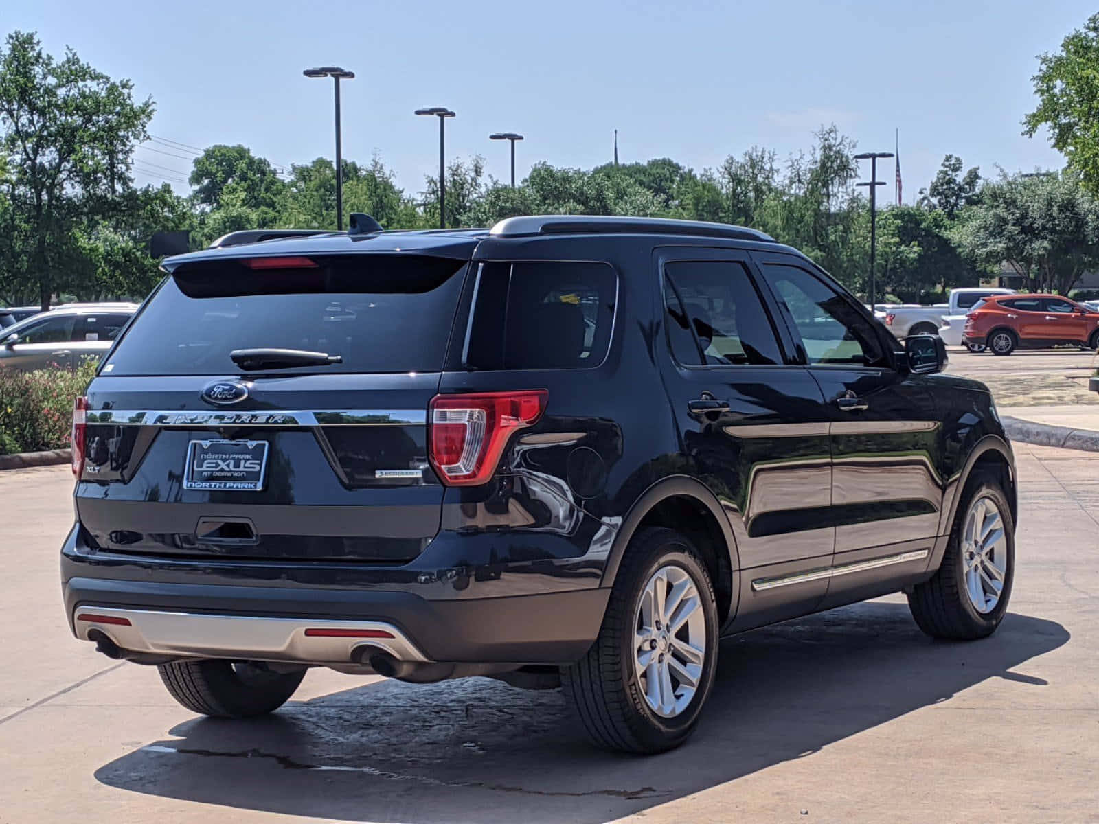 Ford Explorer 桌布 壁紙 — 一輛亮黑色福特Explorer SUV停放在陽光明媚的經銷商場地上，背景有樹木和其他汽車。