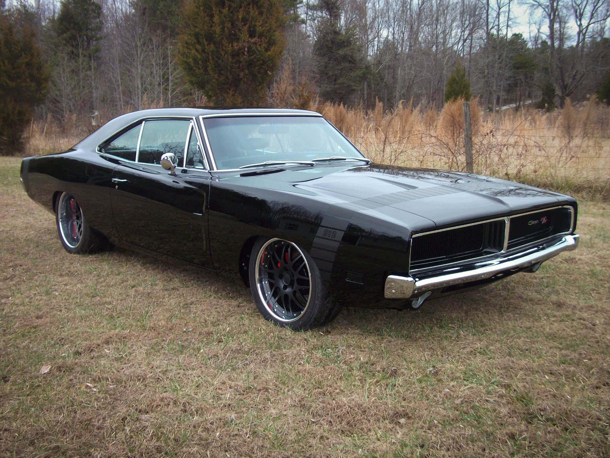 Dodge 桌布 壁紙 — 一輛亮黑色經典肌肉車配備訂製輪圈，停泊在樹林附近的乾草地上。